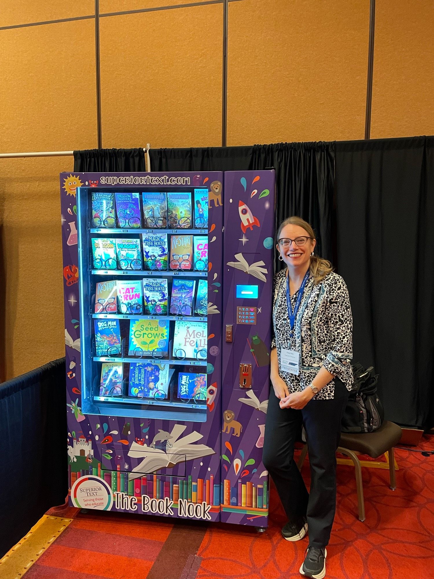 A tall white woman in glasses (me) stands next to a book vending machine.