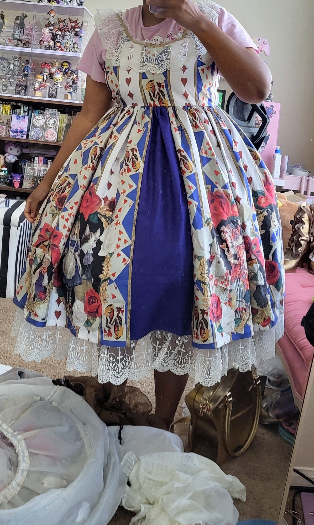 Milkcircus standing in front of a mirror with various clothes on the floor. They're wearing a white lolita dress with a large full skirt.