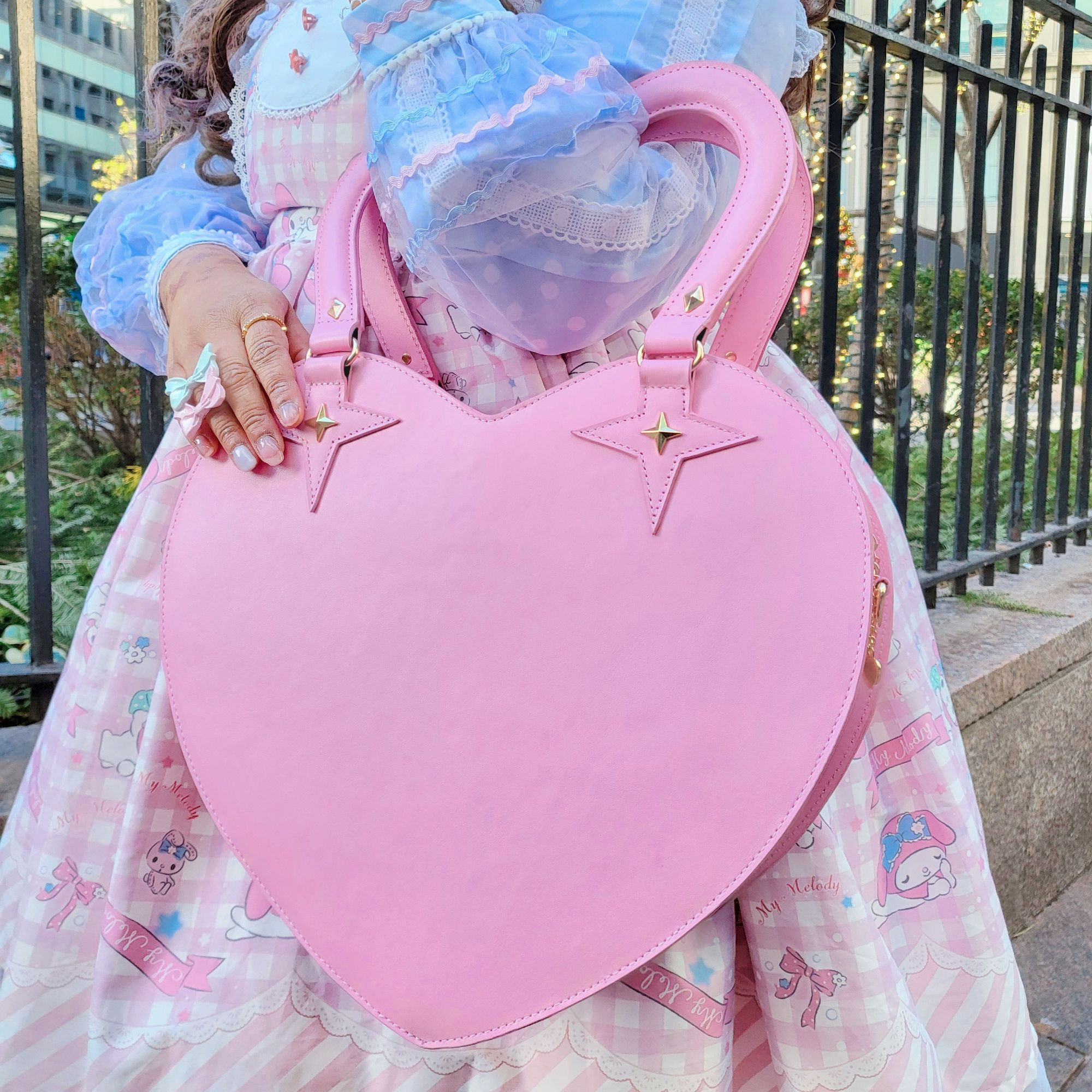 A lolita holding a large pink heart shaped bag with a heart shaped handle.