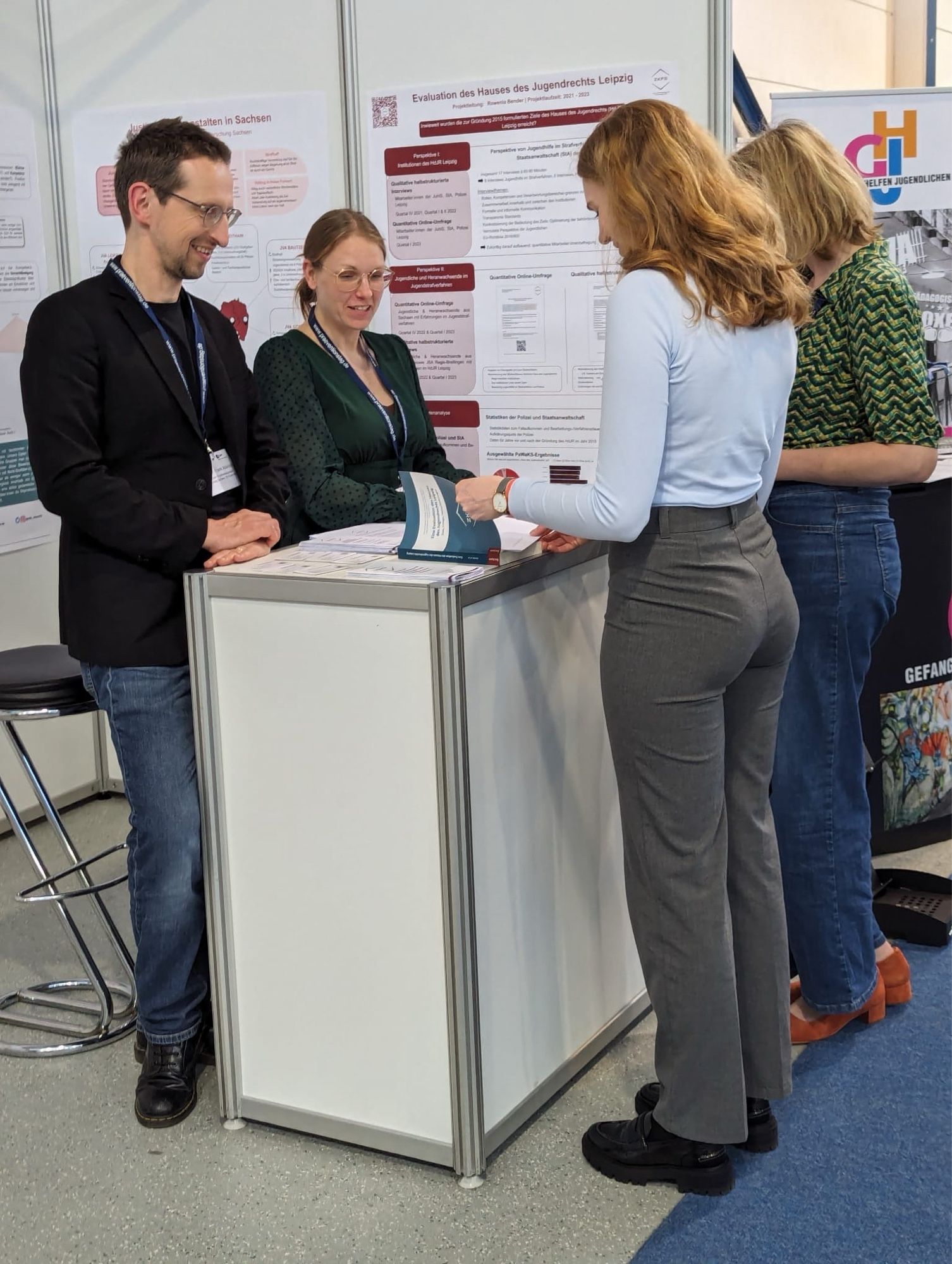 Vier Personen sprechen an einem Infostand auf einer Tagung.