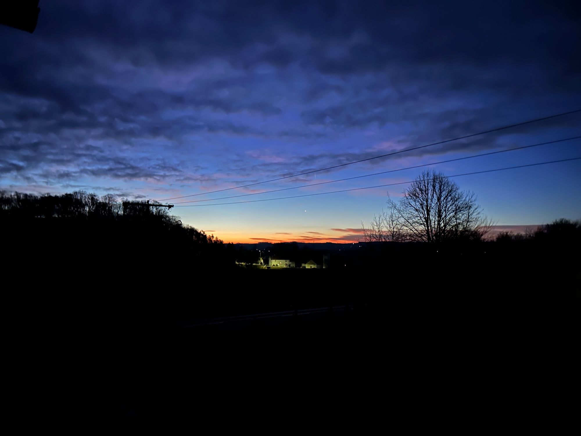 Sunrise in a deep blue sky. Some soft clouds above trees in the shadow.