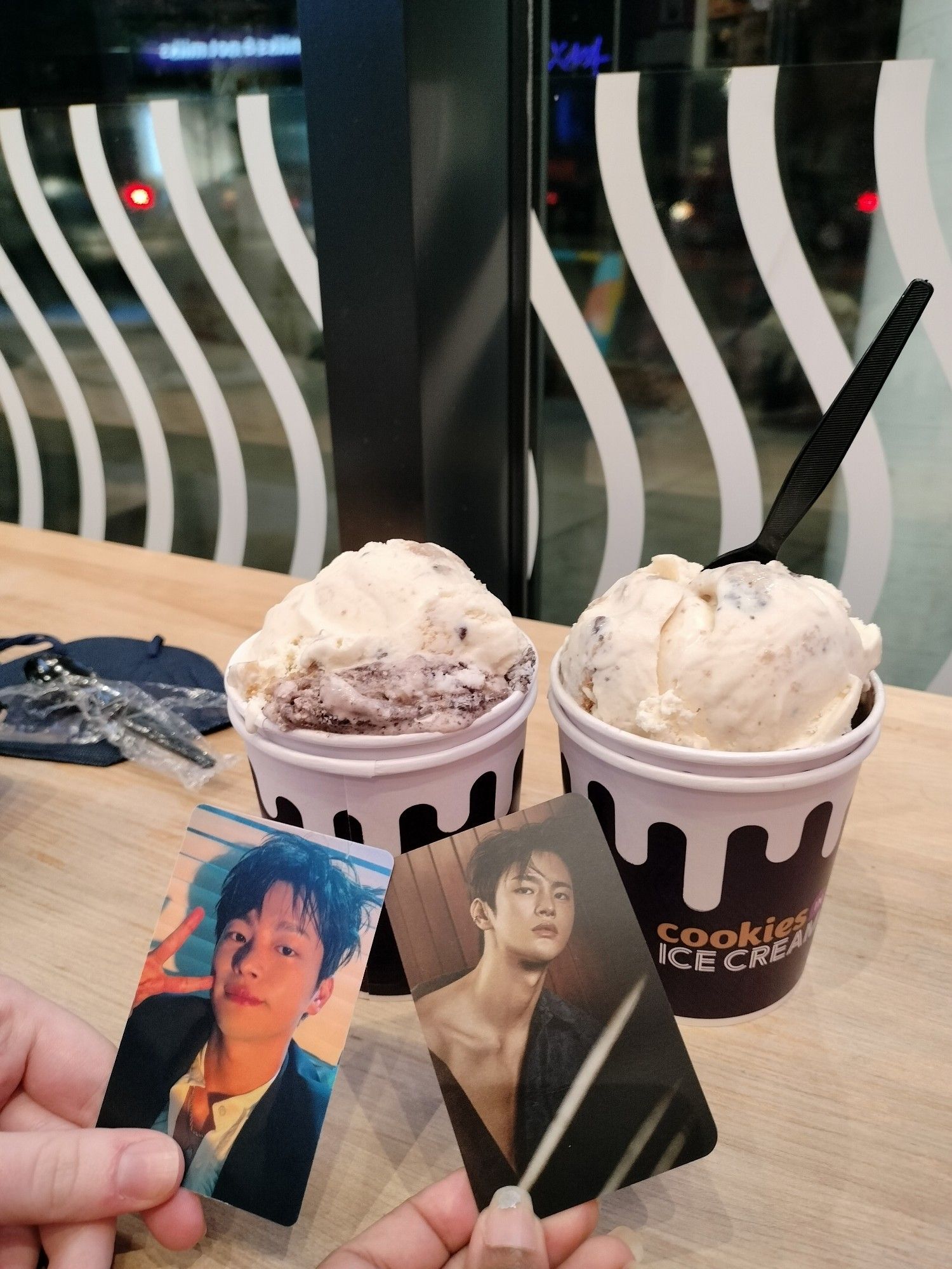 A picture of two hands holding photocards with two cups of ice cream in the background