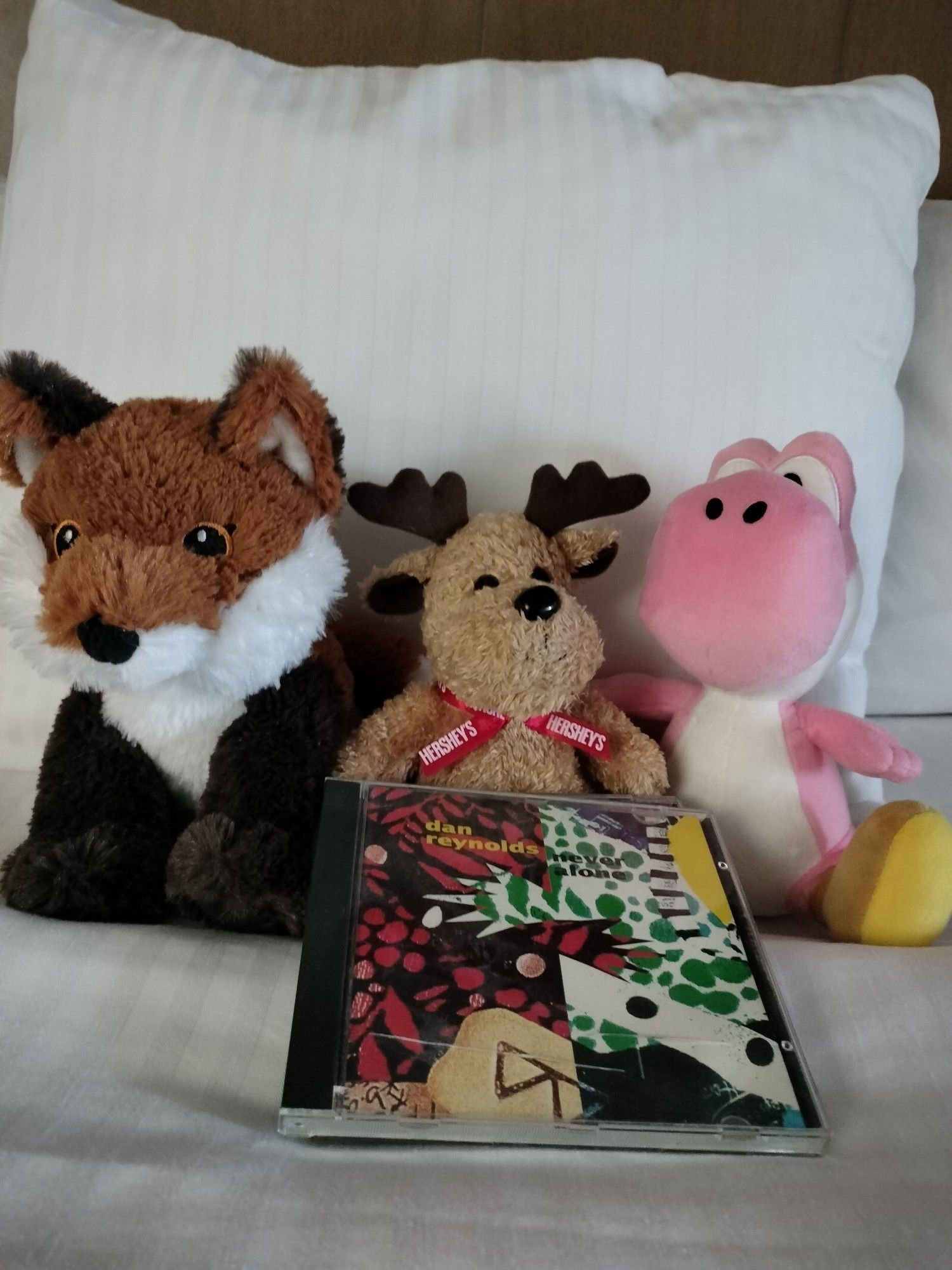 A picture of different plushies from left to right, a fox plushie, a moose plushie, and Yoshi plushie. In front of the plushies are two CDs