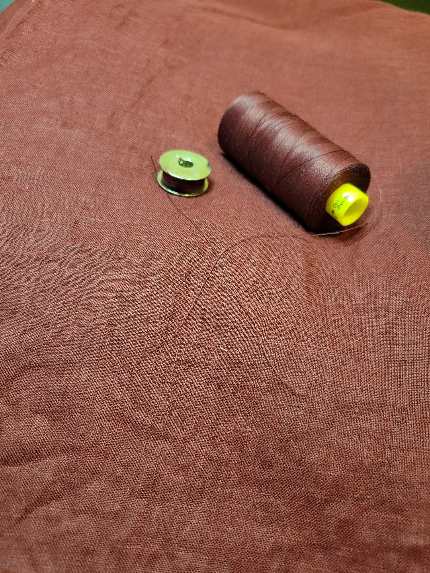 Red linen with a silver sewing machine bobbin and matching red thread set on top.