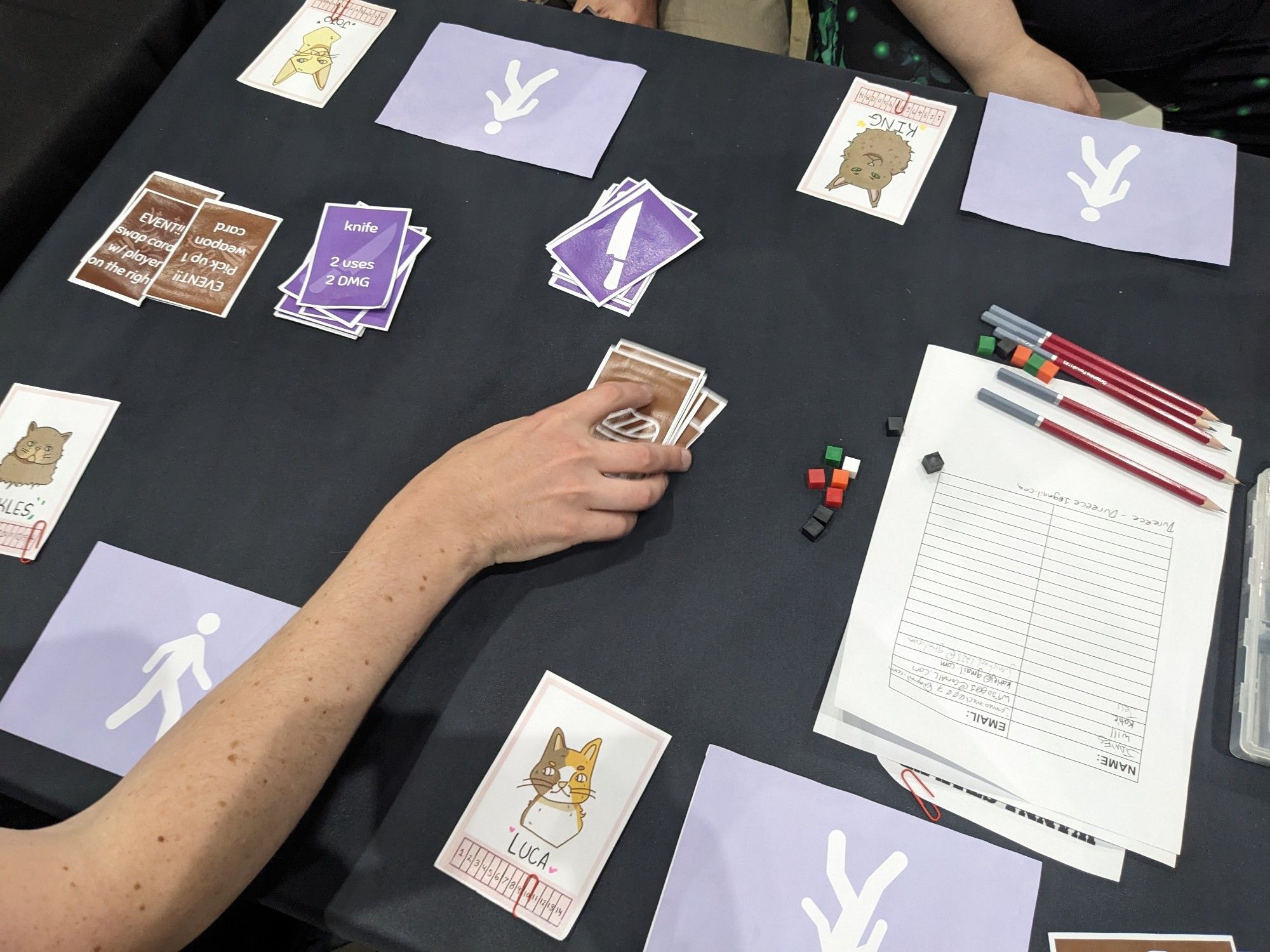 A playtest card game involving cannibal cats vying for adoption. Someone is holding the deck of meat cards.