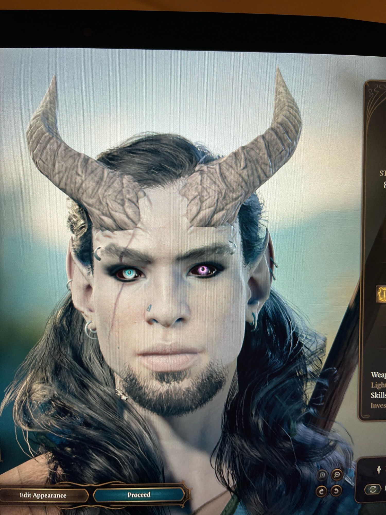 BG3 Theibrin, white “tiefling” with long black hair with one blind eye with black sclera and one lavender eye with black sclera. He has numerous piercings and pointed ears. His horns aren’t correct but they are the best I could do lol