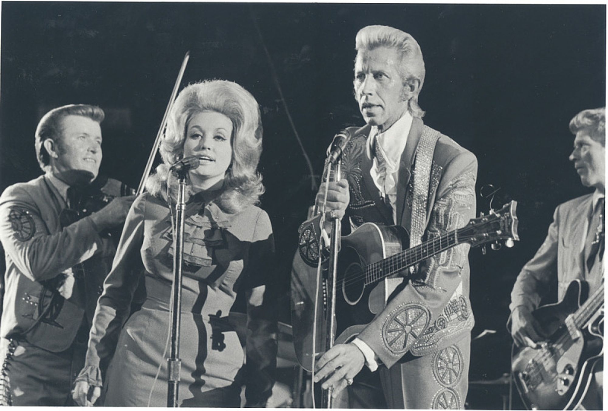 Dolly Parton and Porter Wagner performing with the Wagonmasters in concert 1967. Dolly's hair is piled high and Porter has a phenomenal. blond duck tail hairstyle: hair swept up from the forehead and straight back from the sides with the back extending over the collar.