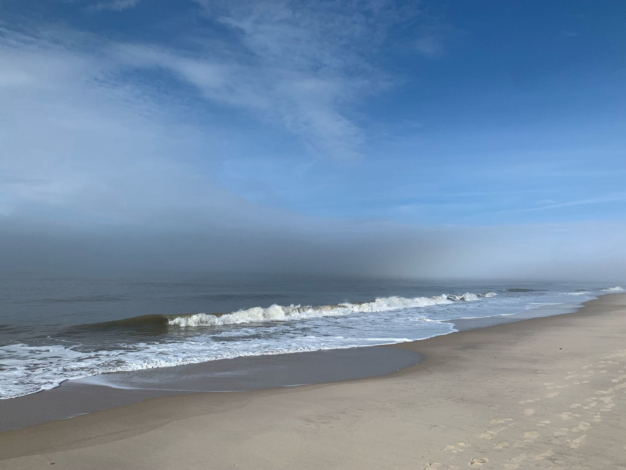 Nordsee und Strand. Leichte Brandung. Horizont dunkel, darüber blauer Himmel.