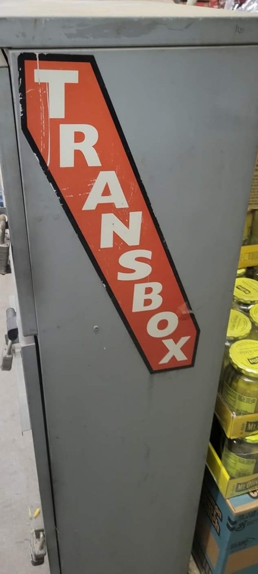 A tall metal box shaped rectangular that says "Transbox" in a diagonal path from top left to bottom right.