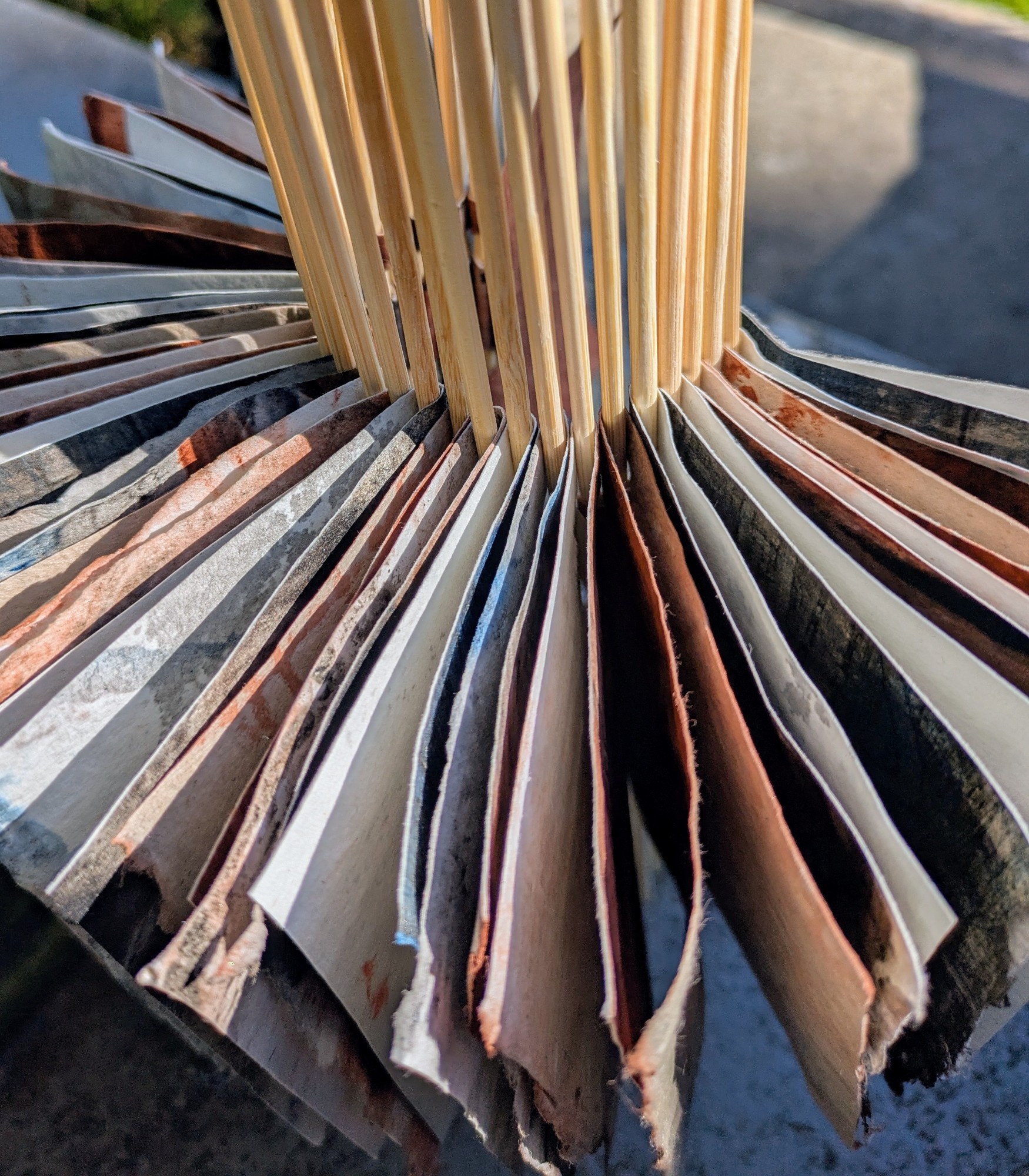 Handmade linen paper bound together in a piano hinge book form with bamboo skewers is pictured standing with the pages open in a sunburst shape. 