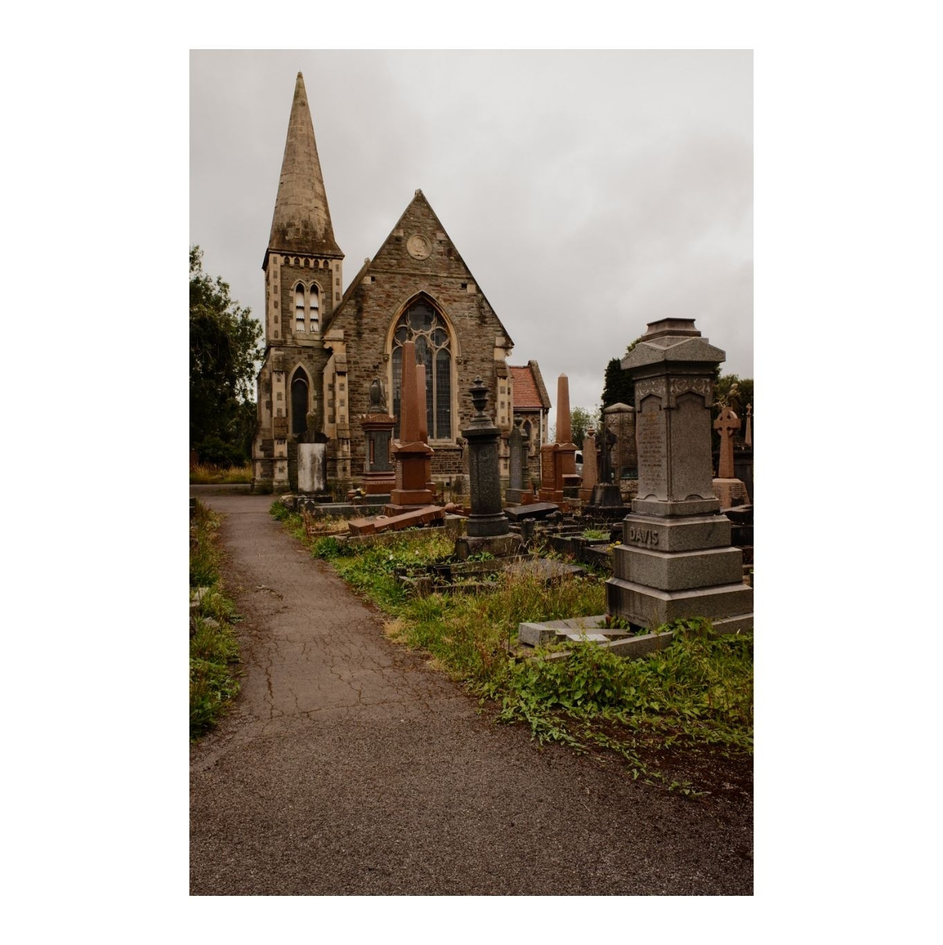 A small Victorian Gothic Chapel in the centre of a cemetery surrounded by ornate tombstones. The sky above is gloomy.