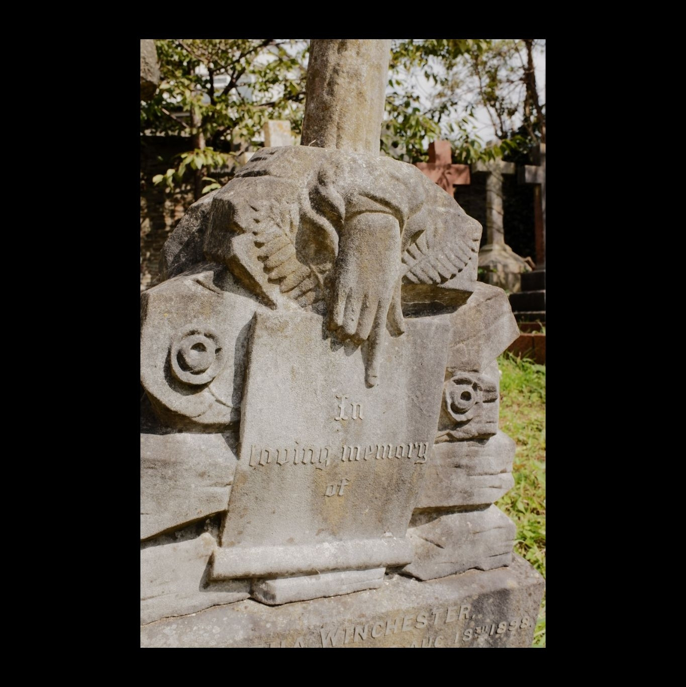 A headstone with a carved manicure (pointing finger) indicating a scroll with the words “in loving memory of”.