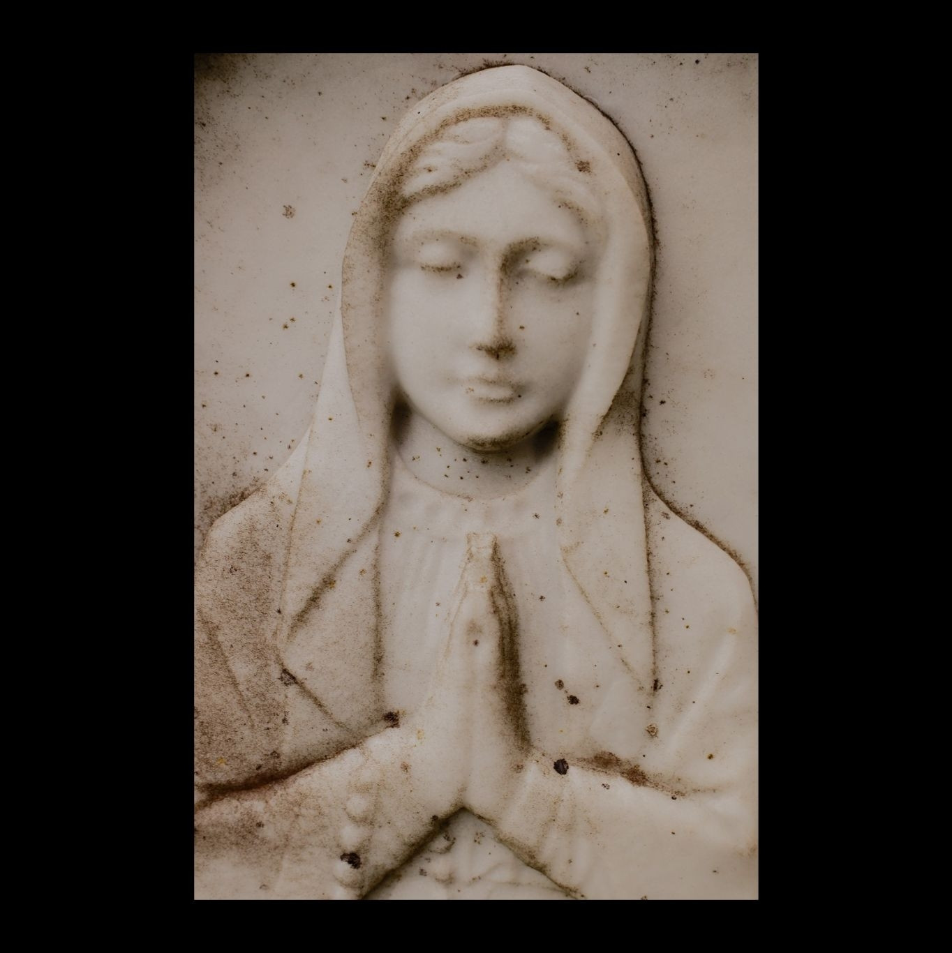 A simple carving on a headstone of a person in a veil at prayer. Is it supposed to be Mary?