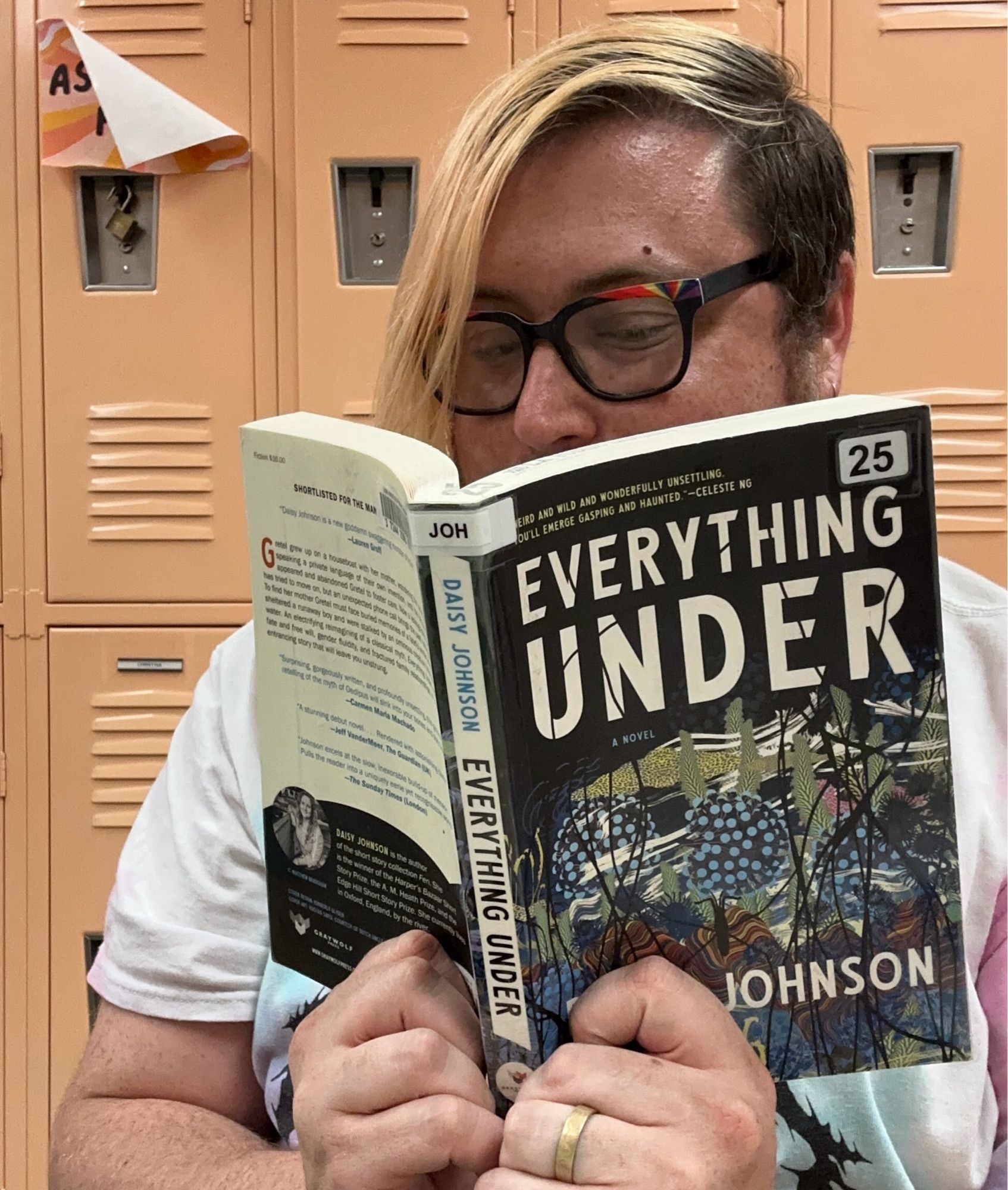 A selfie of Vincey reading, they’re wearing a tie-dye t-shirt. The book opened in front of them and partially obscuring their face is, Everything Under by Daisy Johnson.