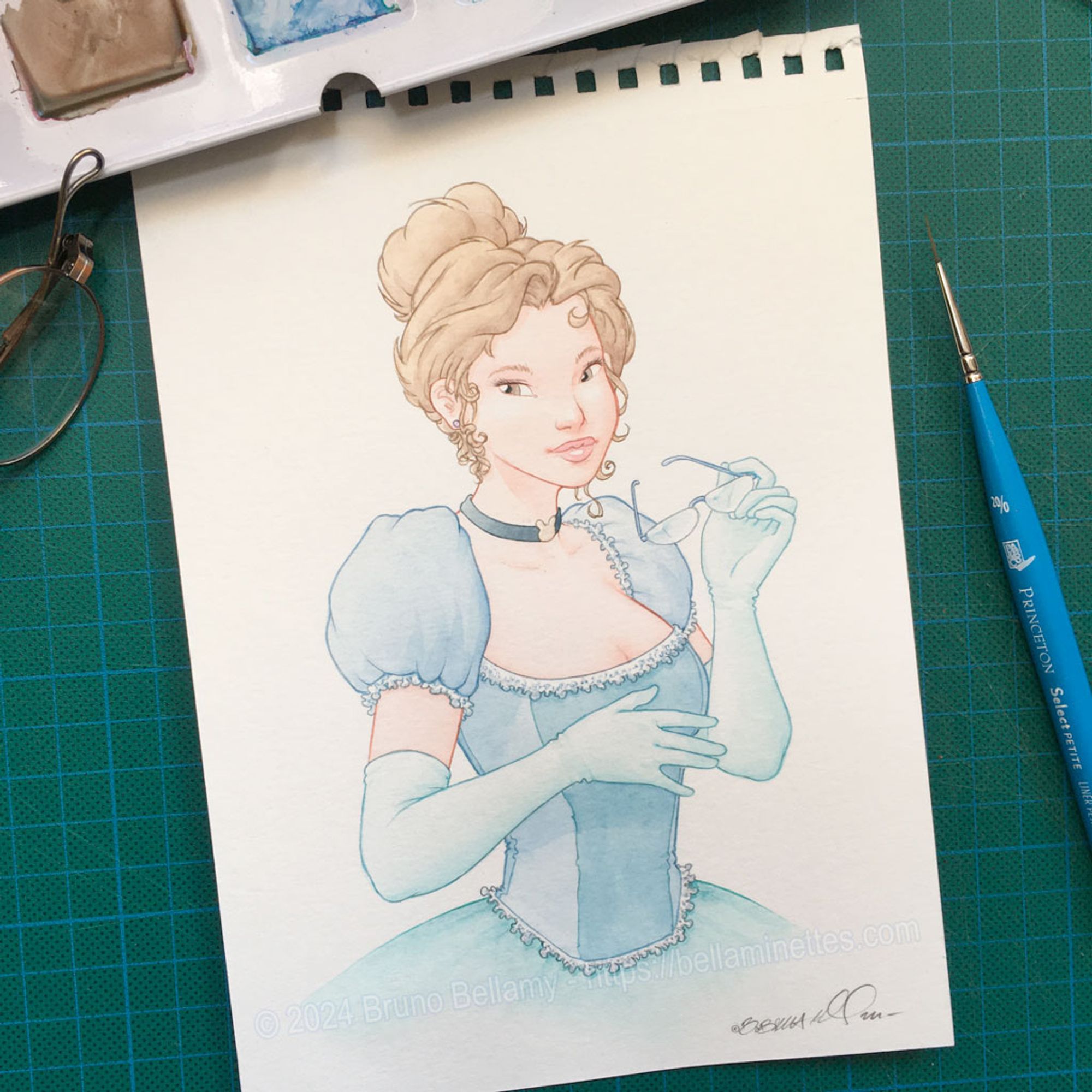 Photo de l'aquarelle tout juste achevée, de cette bellaminette en costume XIXe. On distingue autour de la feuille, sur ma table à dessin, un bout de la palette d'aquarelles, de mes lunettes, et du pinceau très fin qui a servi à repasser les traits de contour à la couleur…