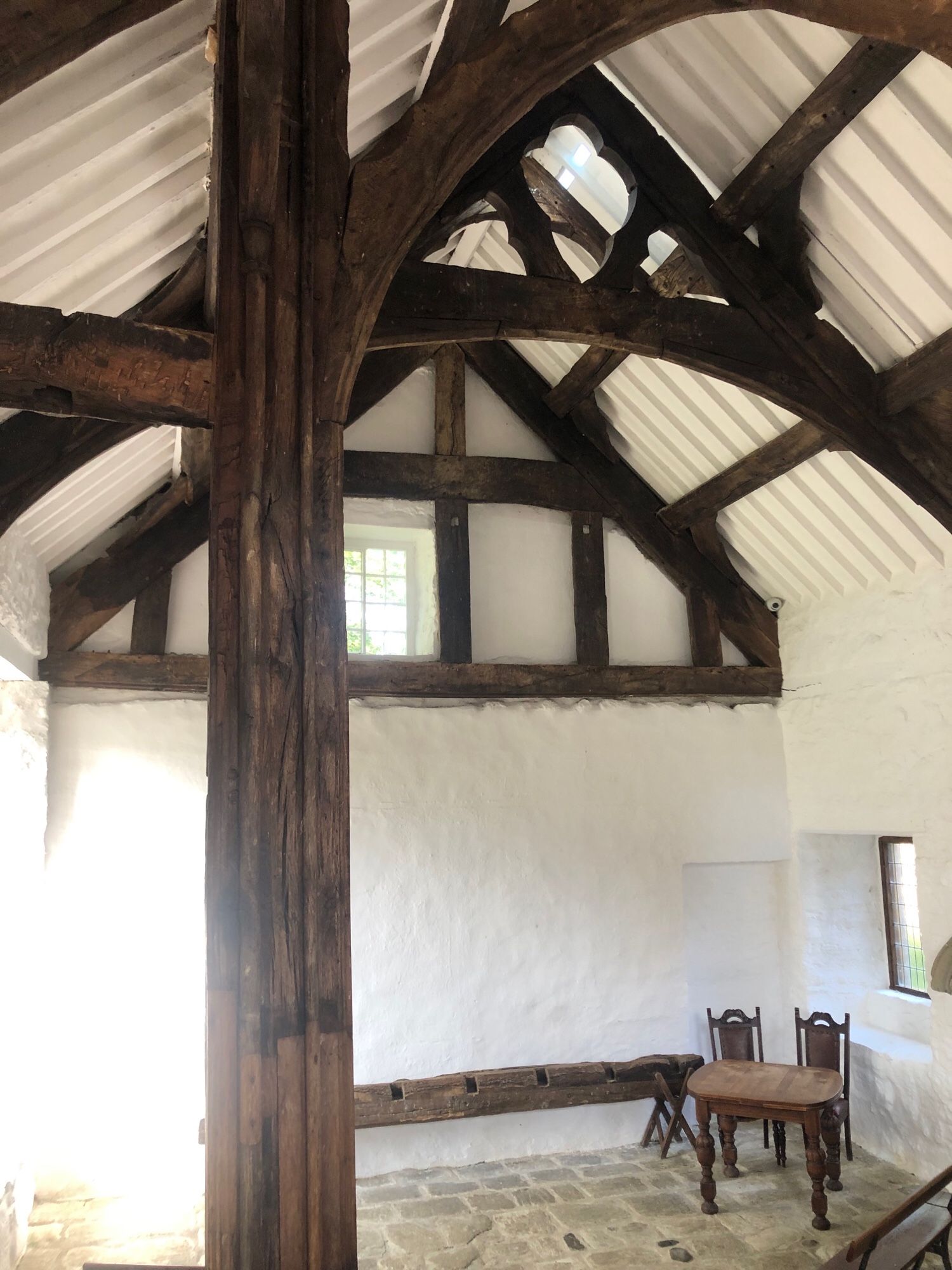 Empty white medieval hall with high ceiling and wooden beams. Two chairs and a table in the corner. Stone floor.