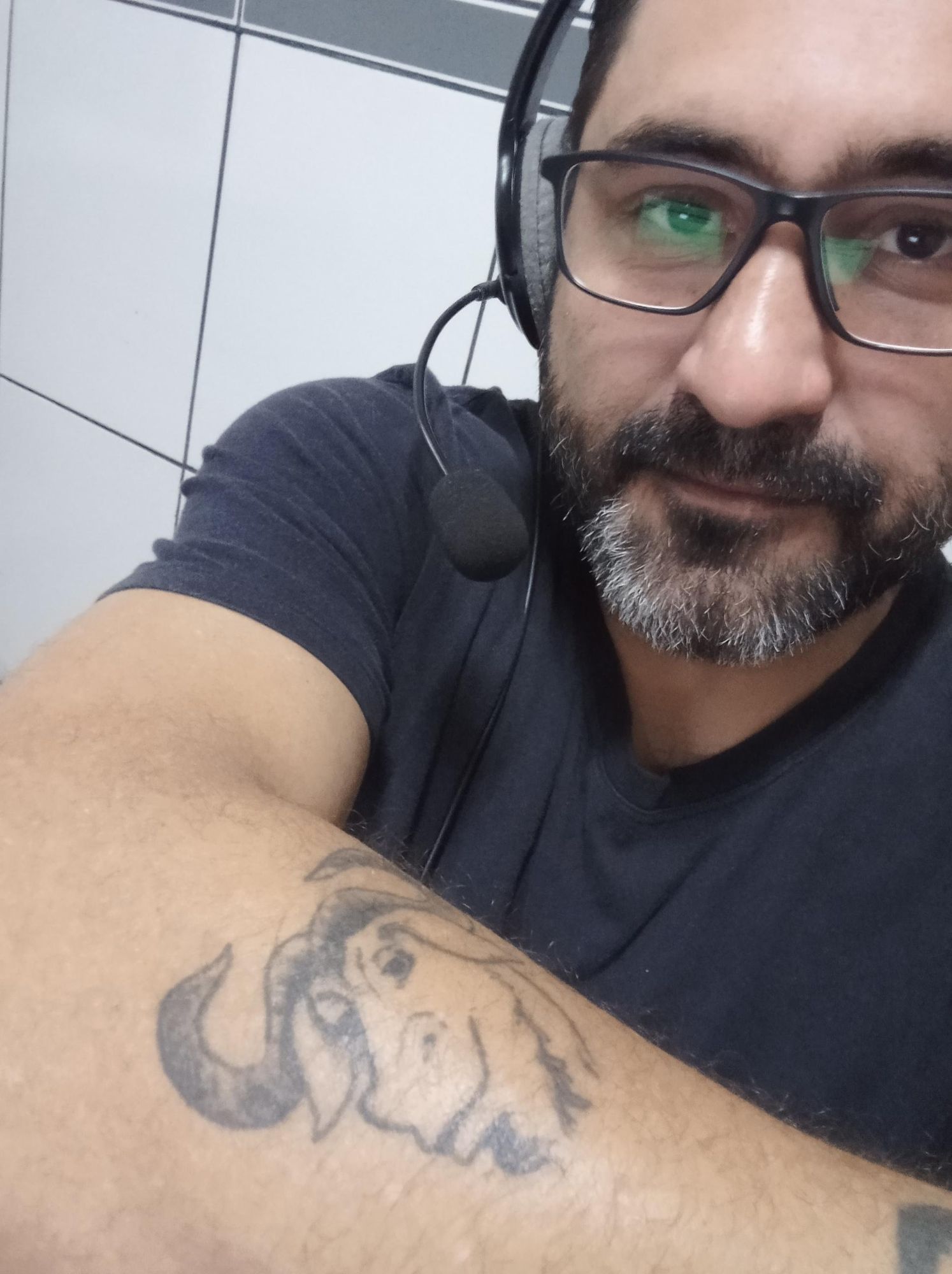 Foto do meu antebraço mostrando a tatuagem do gnu que simboliza o Projeto GNU. Também aparece meu rosto envolto em um headset e minha barba grisalha.