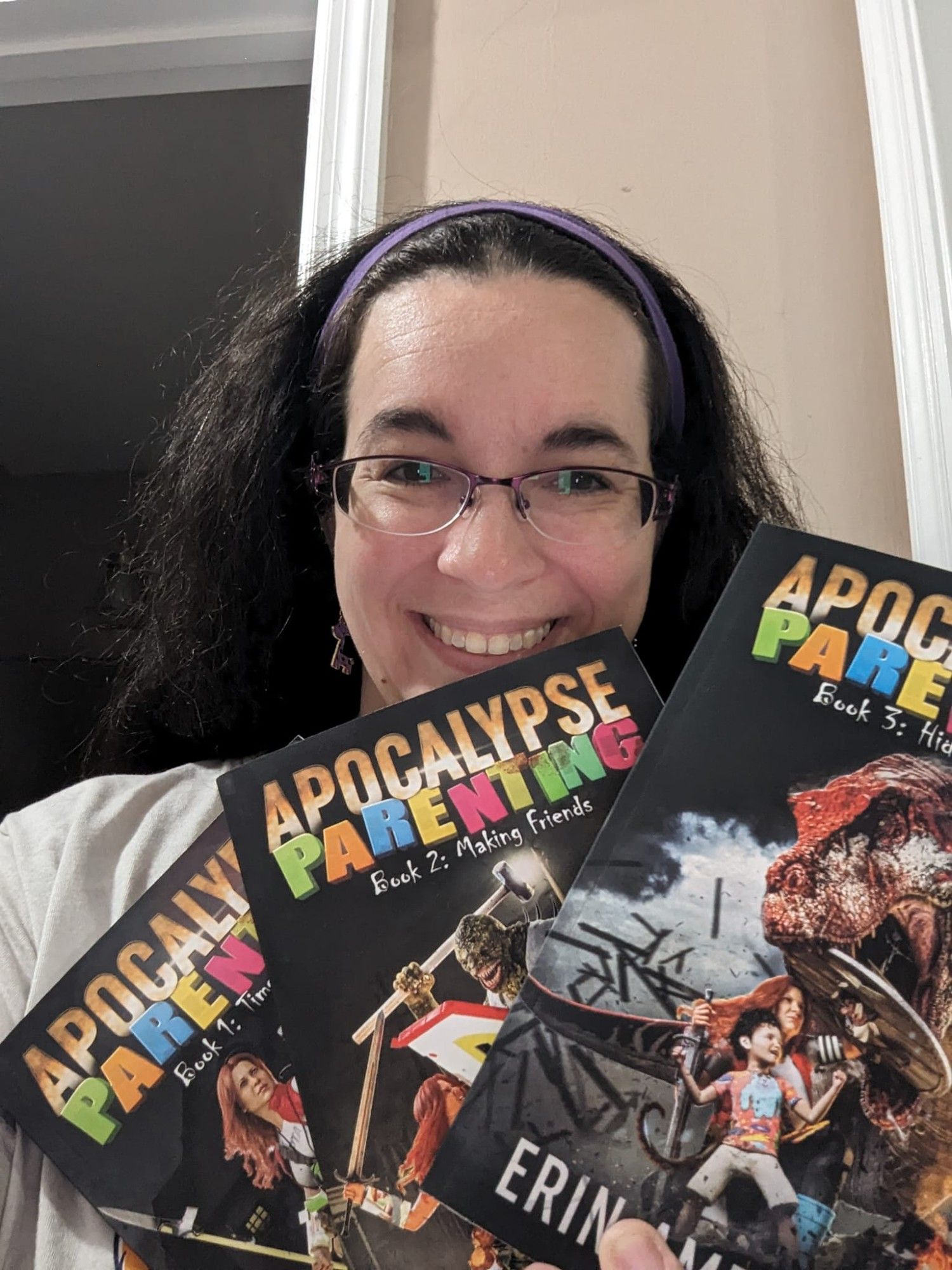 Photo of Erin Ampersand holding print copies of the first three books of Apocalypse Parenting