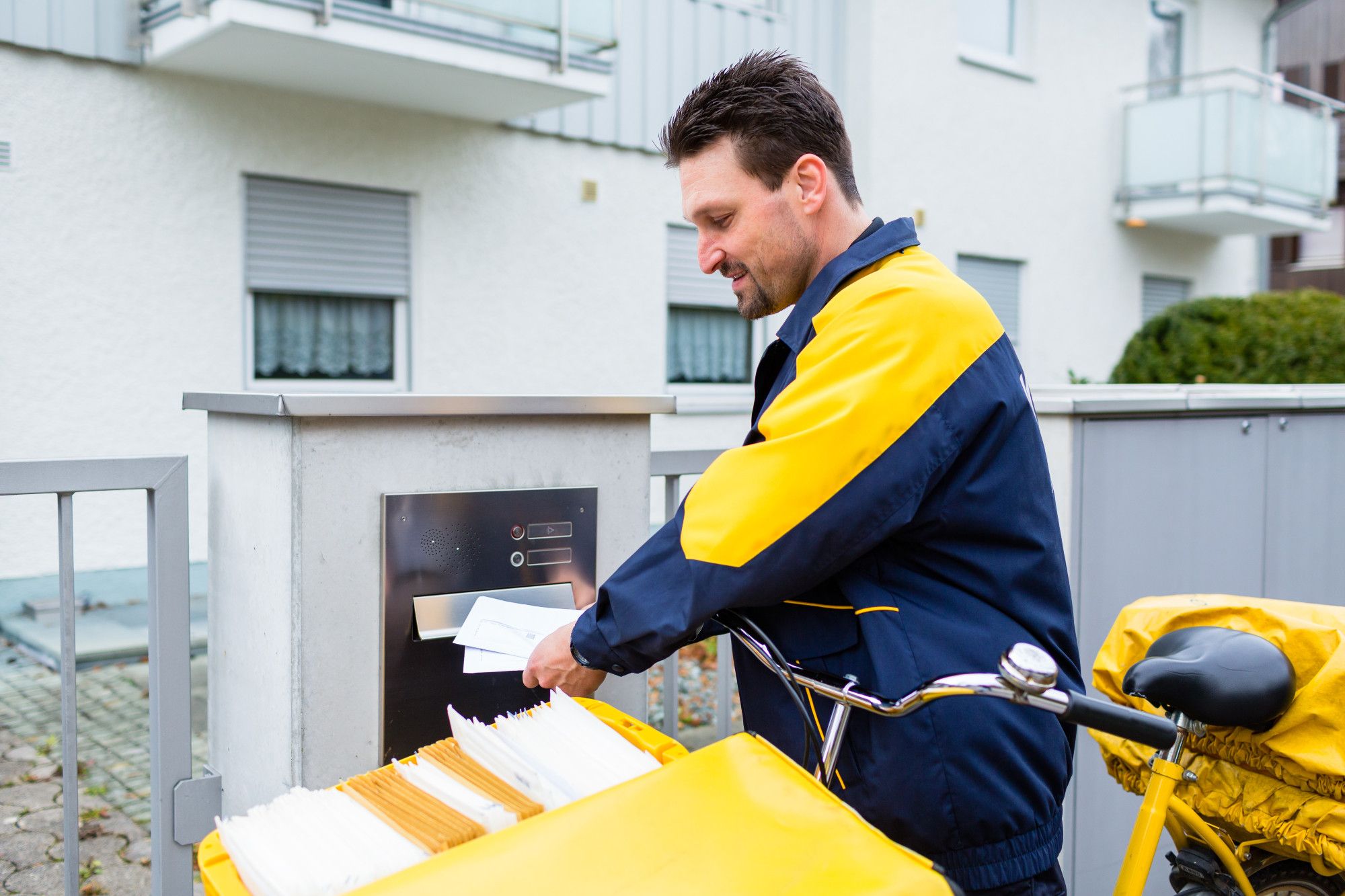 Im Bild: Ein Postbote wirft einen Brief in einen Briefkasten. Foto: kzenon – Shutterstock.