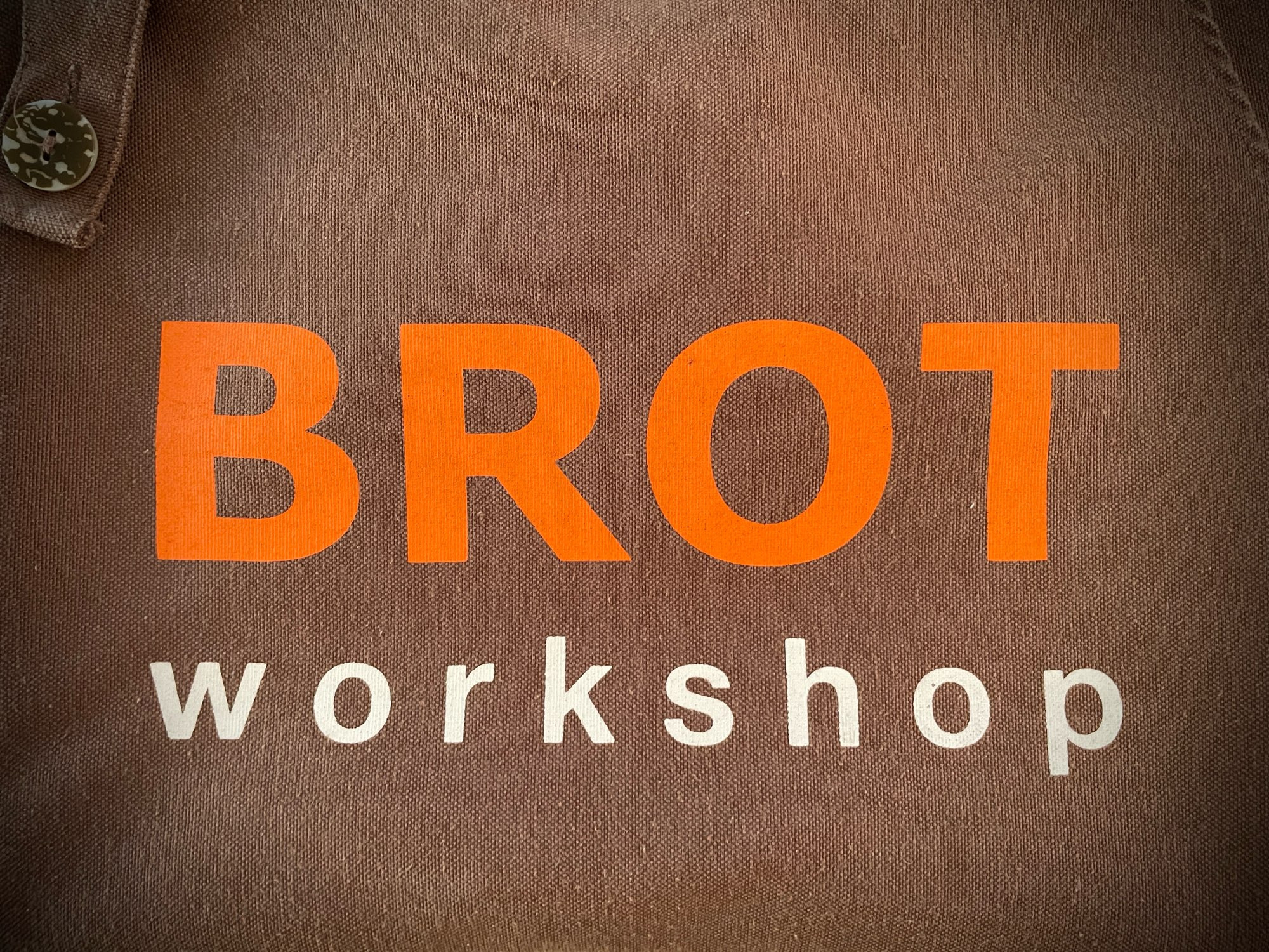 A brown cloth apron with the BROTworkshop insignia printed on the front.