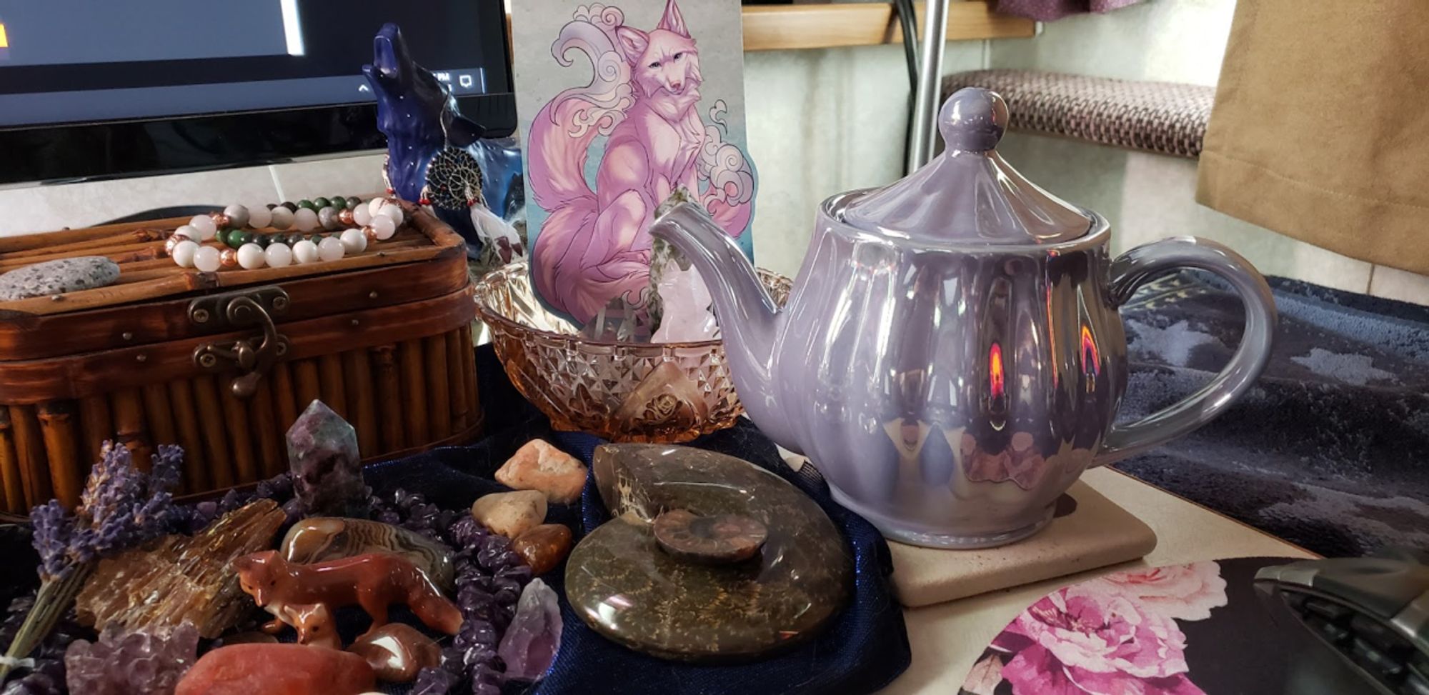 Purple pearlescent teapot on desk with a lot of stones and fox things.