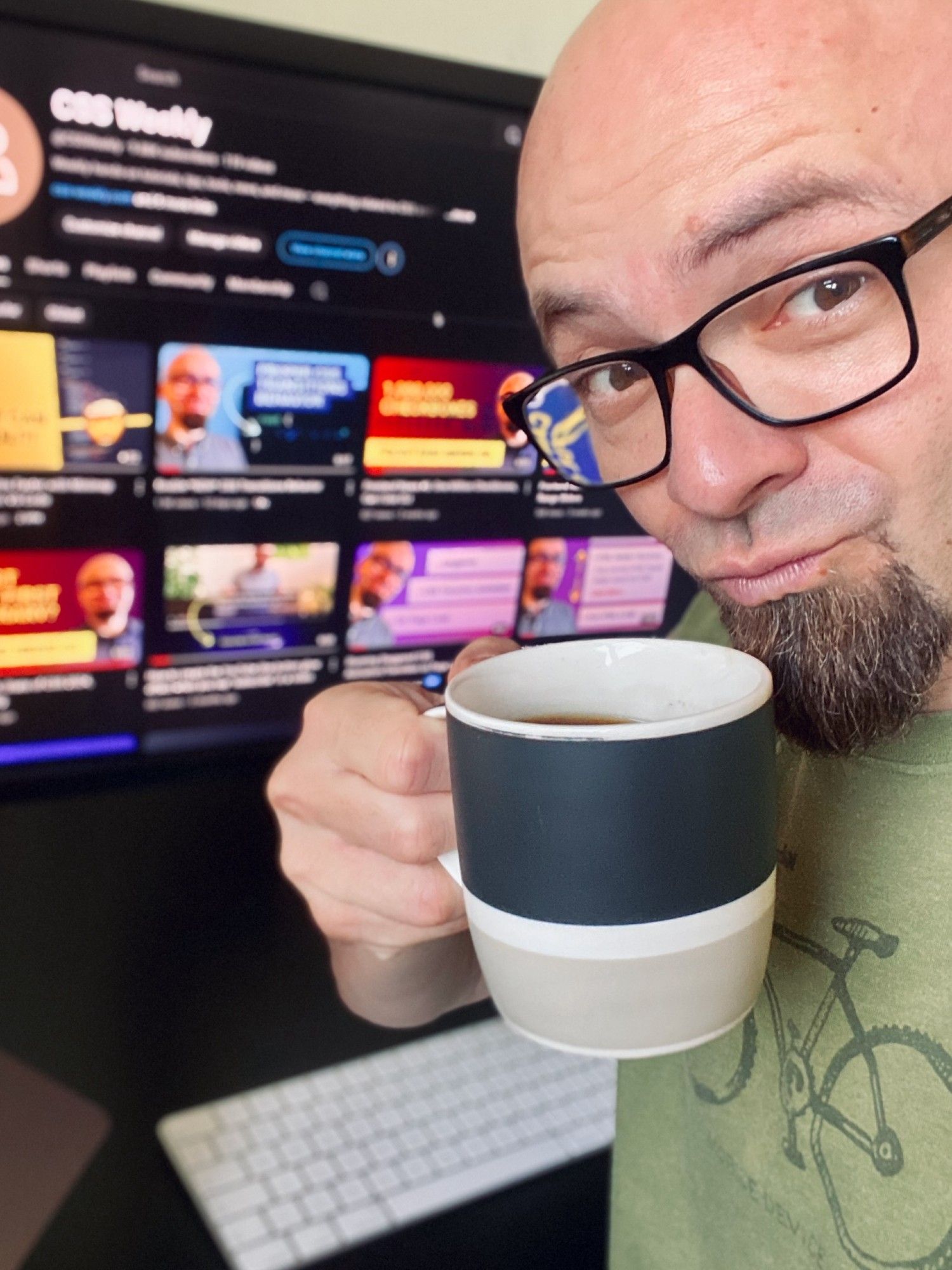 Zoran Jambor holding a cup of coffee in front of a screen showing CSS Weekly YouTube channel.