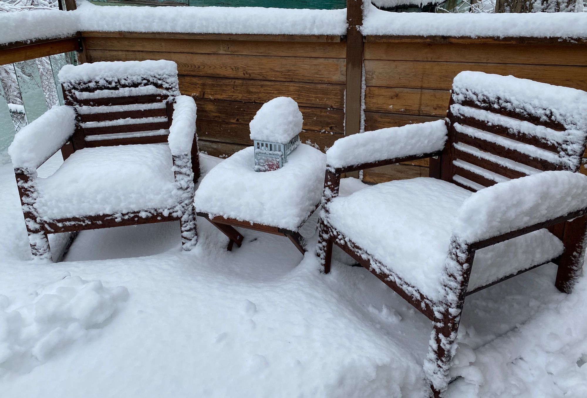 Two outdoor chairs sitting on a back deck, everything covered in 10 inches of snow