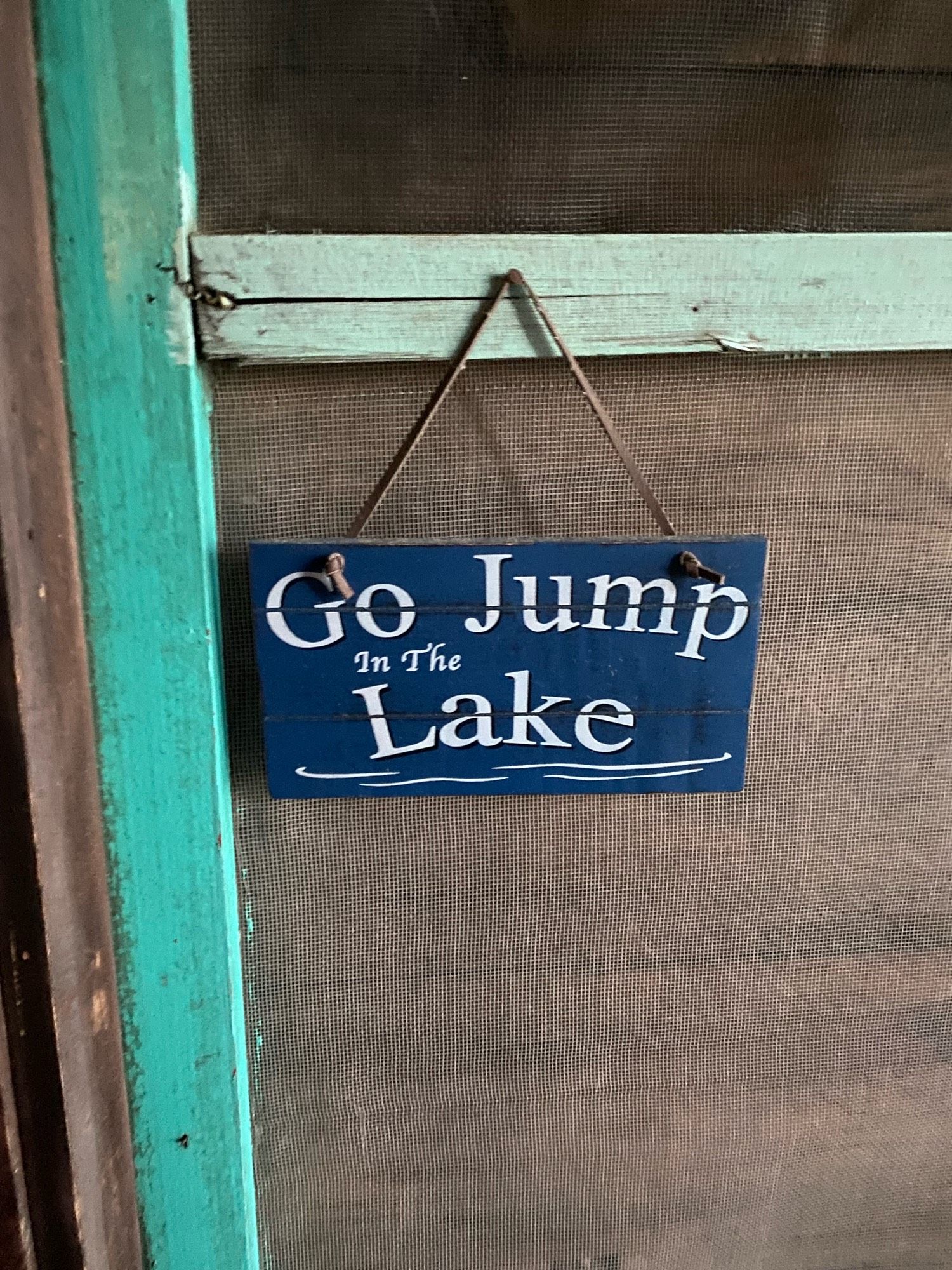 A rustic sign hanging on a cottage wall, saying, “Go jump in the lake.”