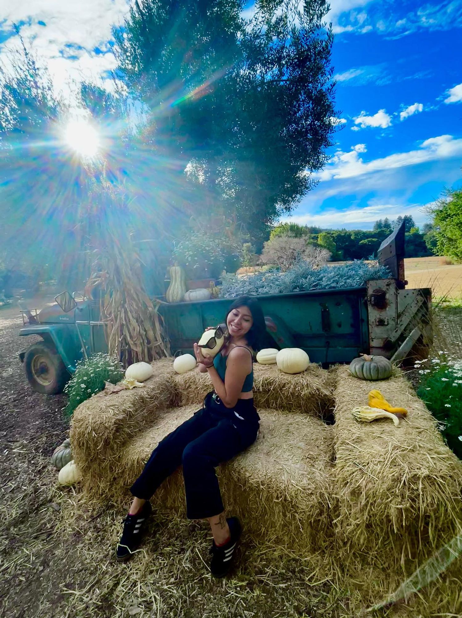 Photo of me in the pumpkin patch, sitting on a couch made of hay in front of a green truck, holding a pumpkin with sunglasses