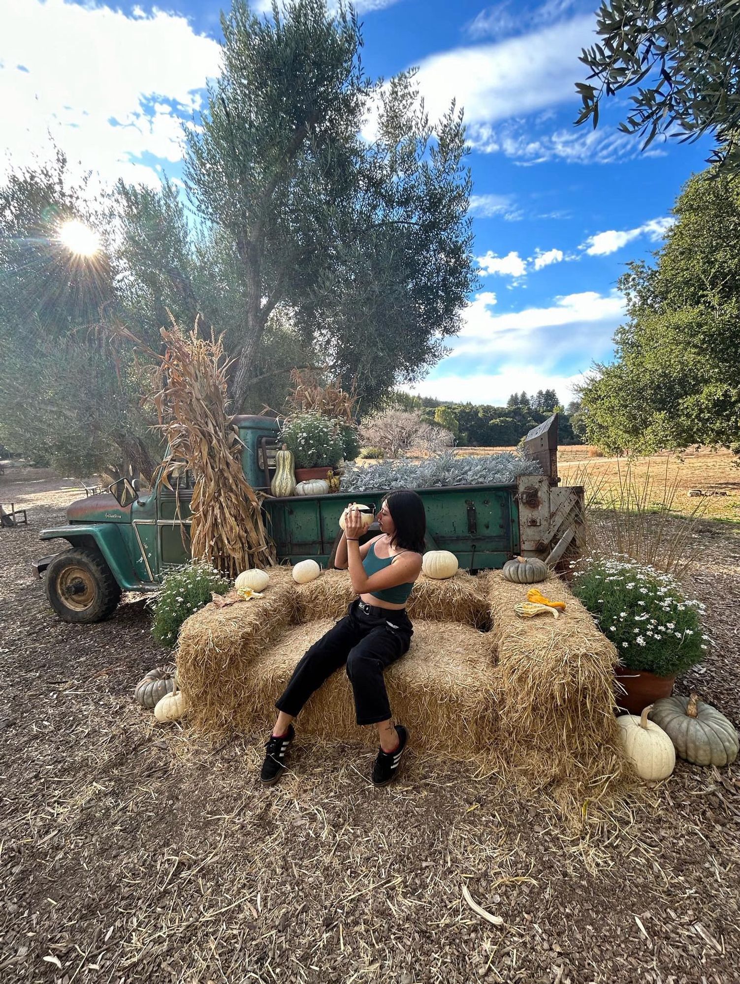 Photo of me in the pumpkin patch, sitting on a couch made of hay in front of a green truck, holding a pumpkin with sunglasses, kissing its nose