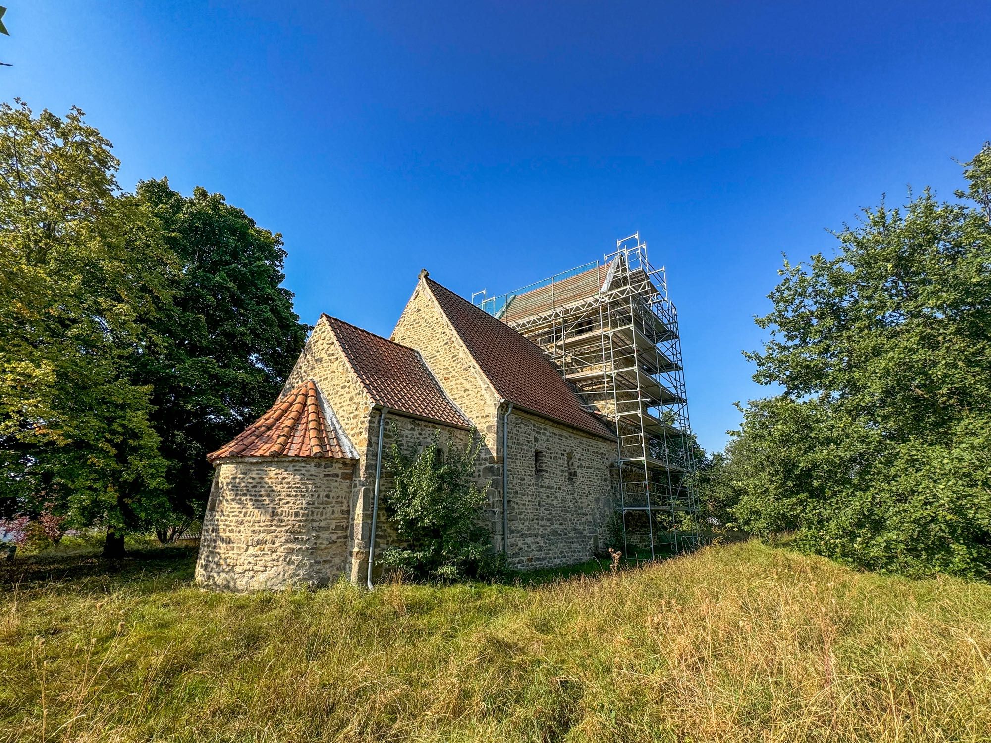 Ein kleine romanische Kirche in Seehausen (Börde) auf grüner Wiese, klassische Vierteilung, Turm, Schiff, Chor und Apsis, Blick von Nordosten, der Turm ist eingerüstet