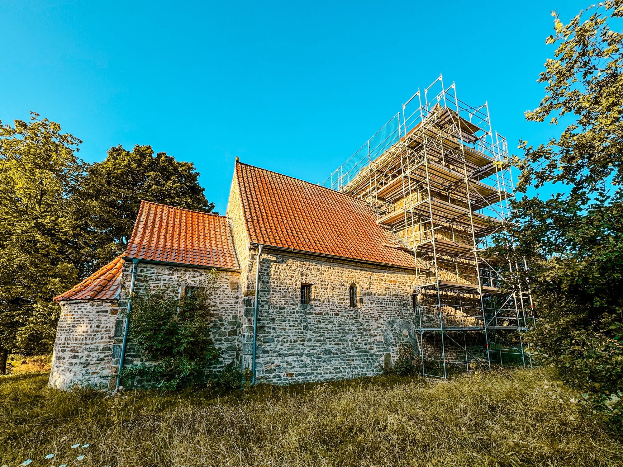 Kleine Romanische Kirche im Feld stehend von Norden gesehen, Gerüst am Turm