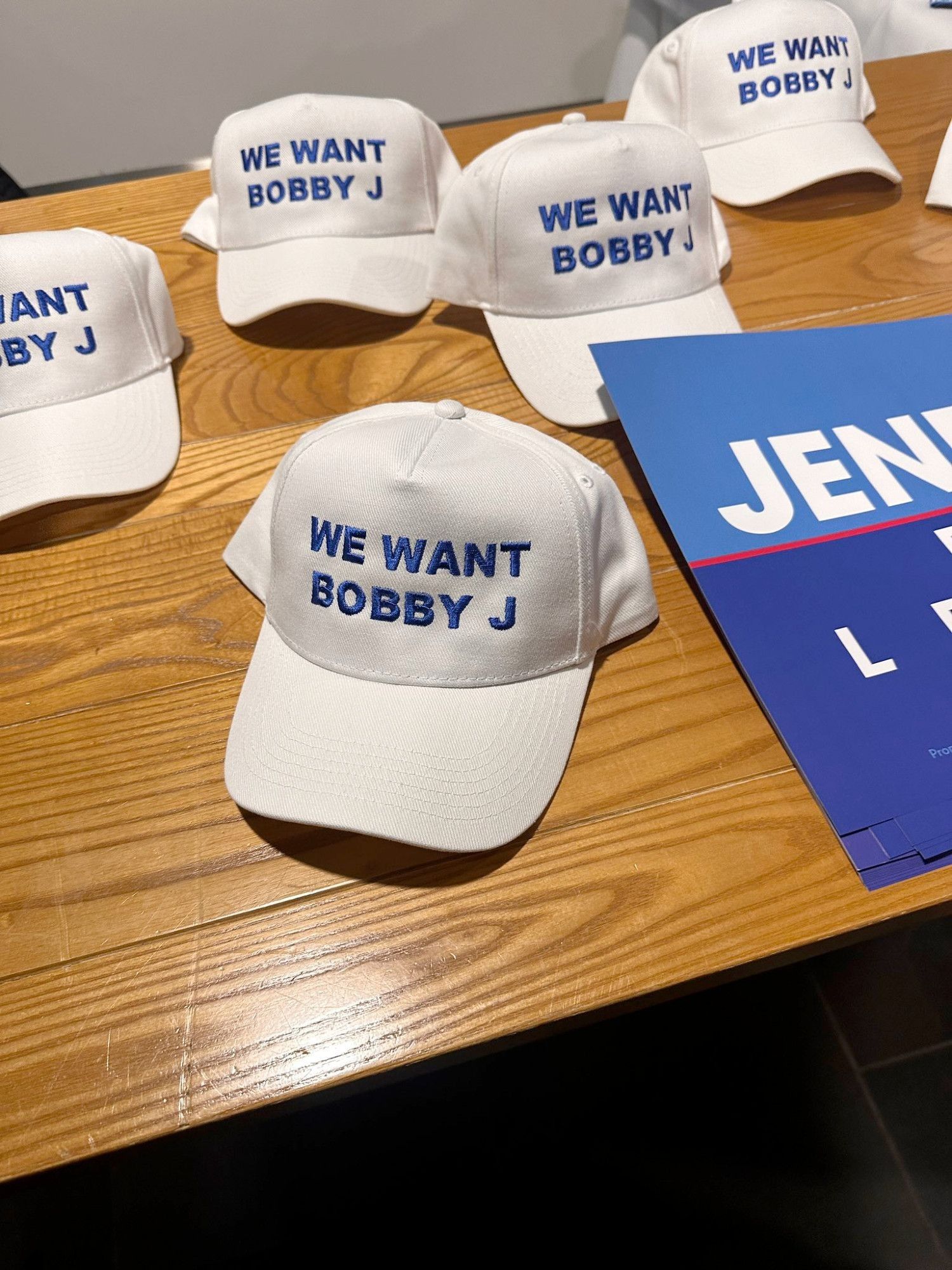 A photo of a bunch of white baseball caps on a table at Tory Party conference. They all say 'We Want Bobby J'