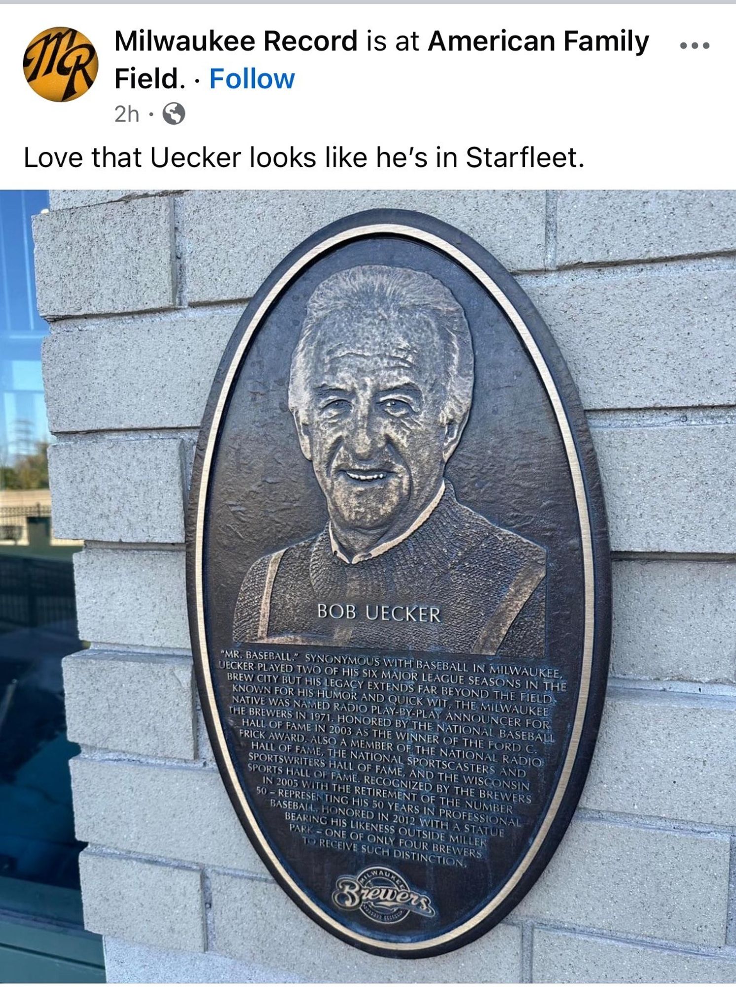 A bronze plaque featuring a relief portrait of Bob Uecker, with text highlighting his contributions to baseball and broadcasting. The plaque is mounted on a wall at American Family Field, home of the Milwaukee Brewers. The post caption reads “Love that Uecker looks like he’s in Starfleet.”