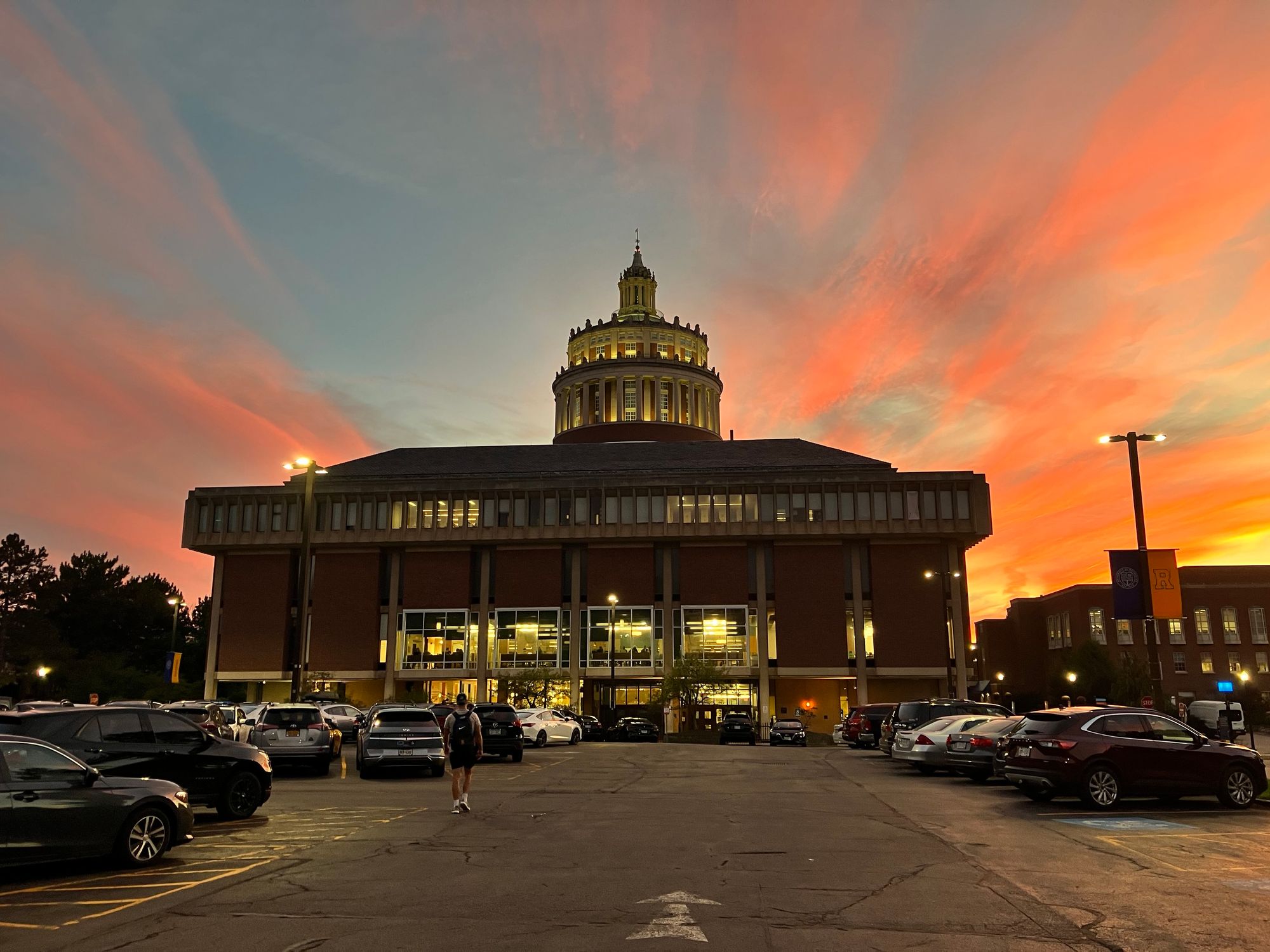 Streaky orange sunset looks like it’s bursting out from behind a library with an ornate bell tower at the top.