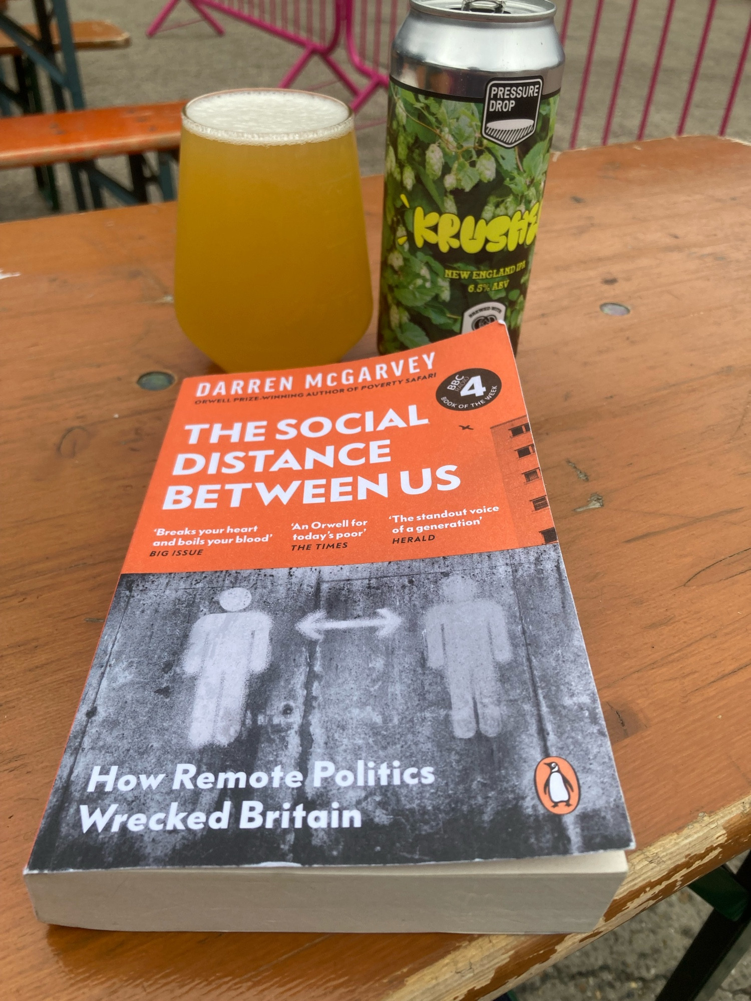 A can of Krusher, a 6.5% New England IPA by Pressure Drop featuring hops on the can and a copy of The Social Distance Between Us by Darren McGarvey.