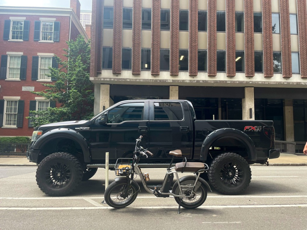 Ebike and a truck, bike is in the foreground and truck is behind it. Truck has a jacked up lift kit