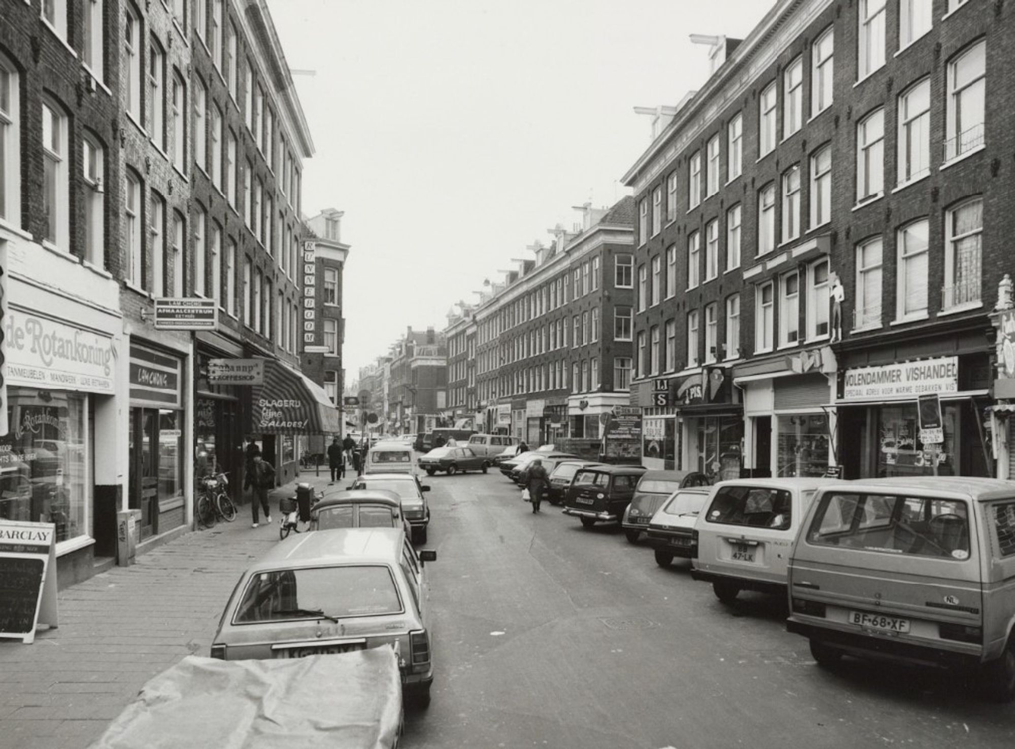 Black and white photo of a street filled w cars and car parking, dingy and skanky
