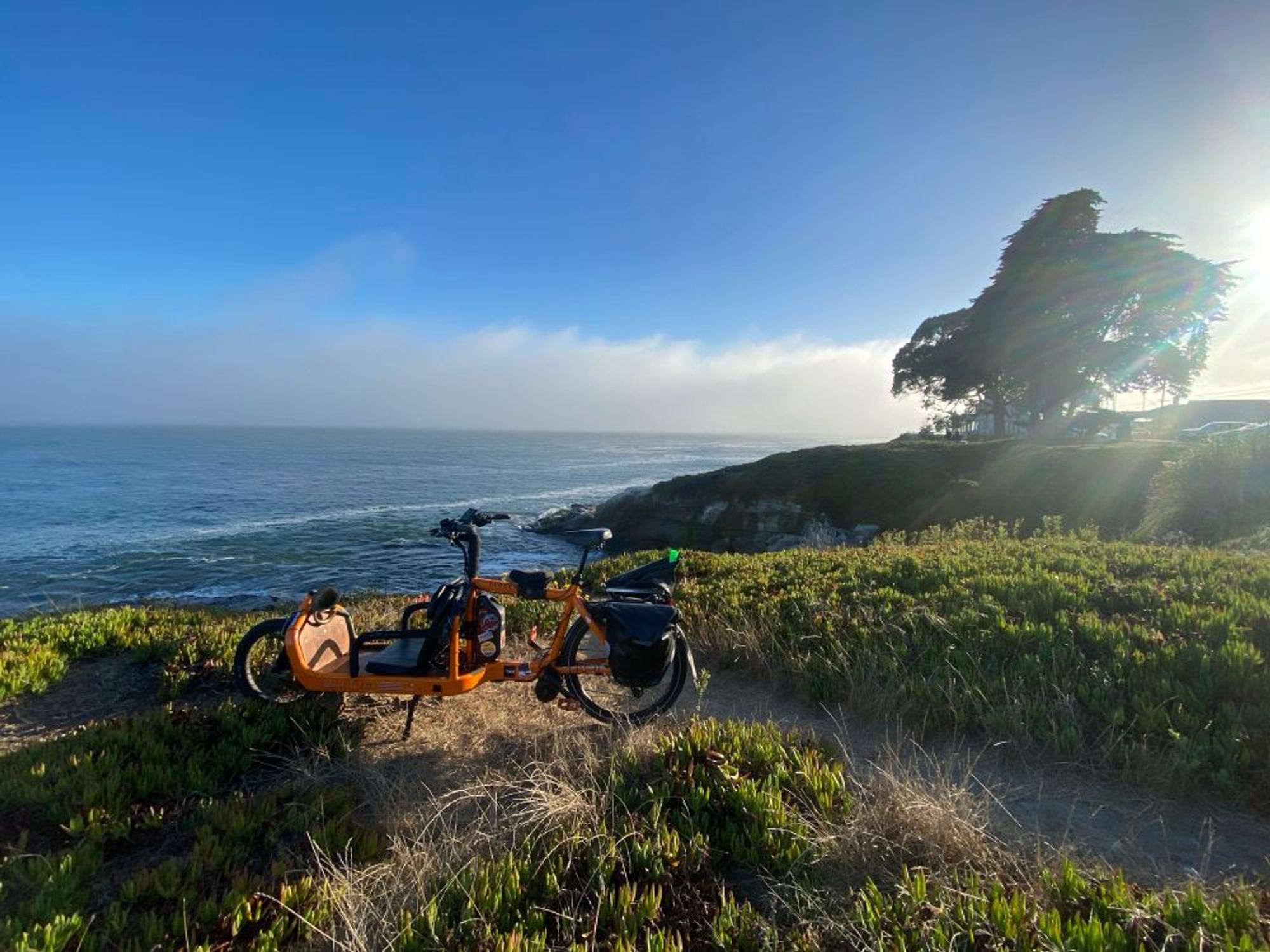 SunnyD bike on a beautiful cliff over looking the ocean, blue sky and sun going down on the right of the screen