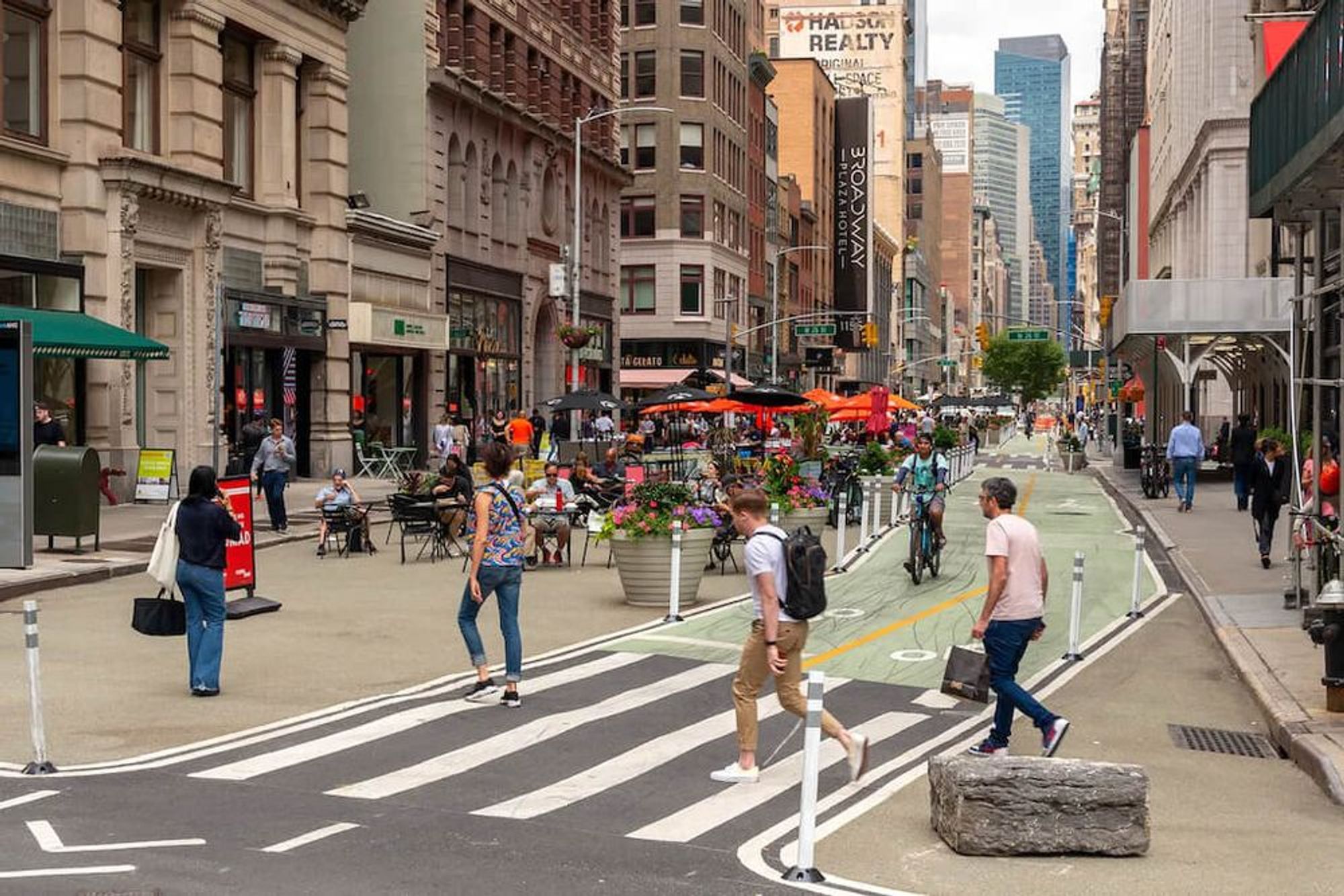 Pedestrianized street in Manhattan, cafe seating, two way bike lane, wide pedestrian crossing with some decent size rocks in the bump out