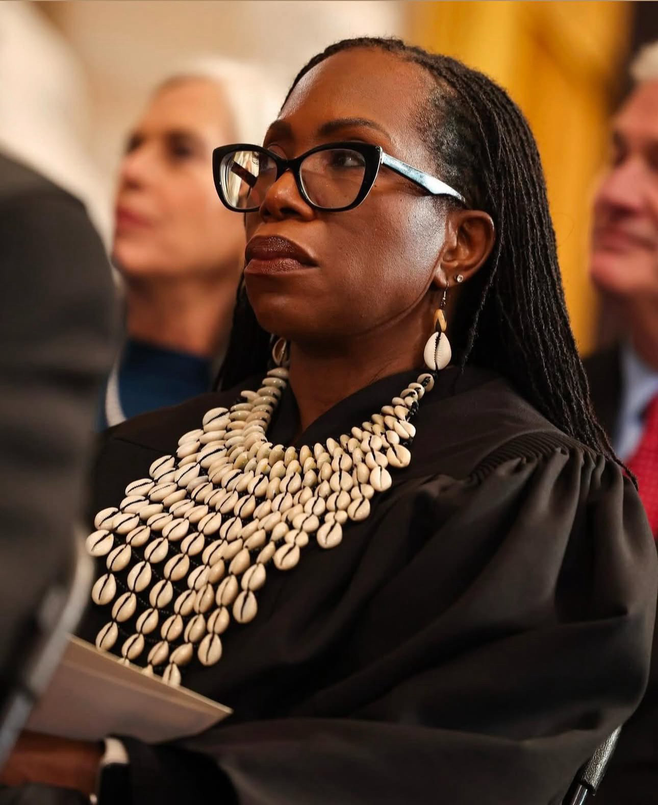 Photograph of Justice Ketanji Brown Jackson, stoic, in a black judge’s robe with ornate Puka shell judge’s collar 