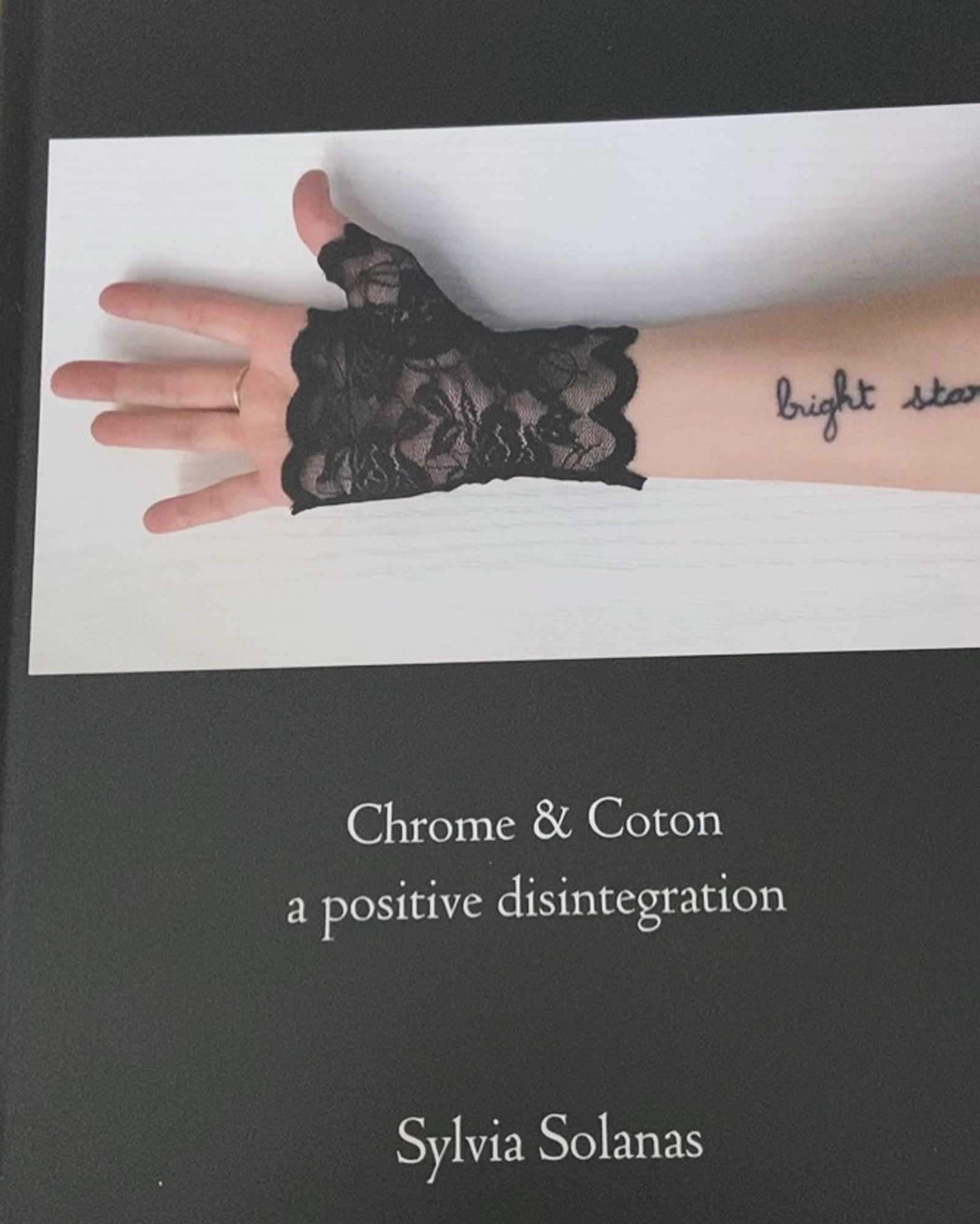 coffee table book “Chrome et Coton, A Positive Disintegration”, by me.
Black cover with an image of my arm, I’m wearing a black lace fingerless glove, we can see my tattoo that reads “bright star”.