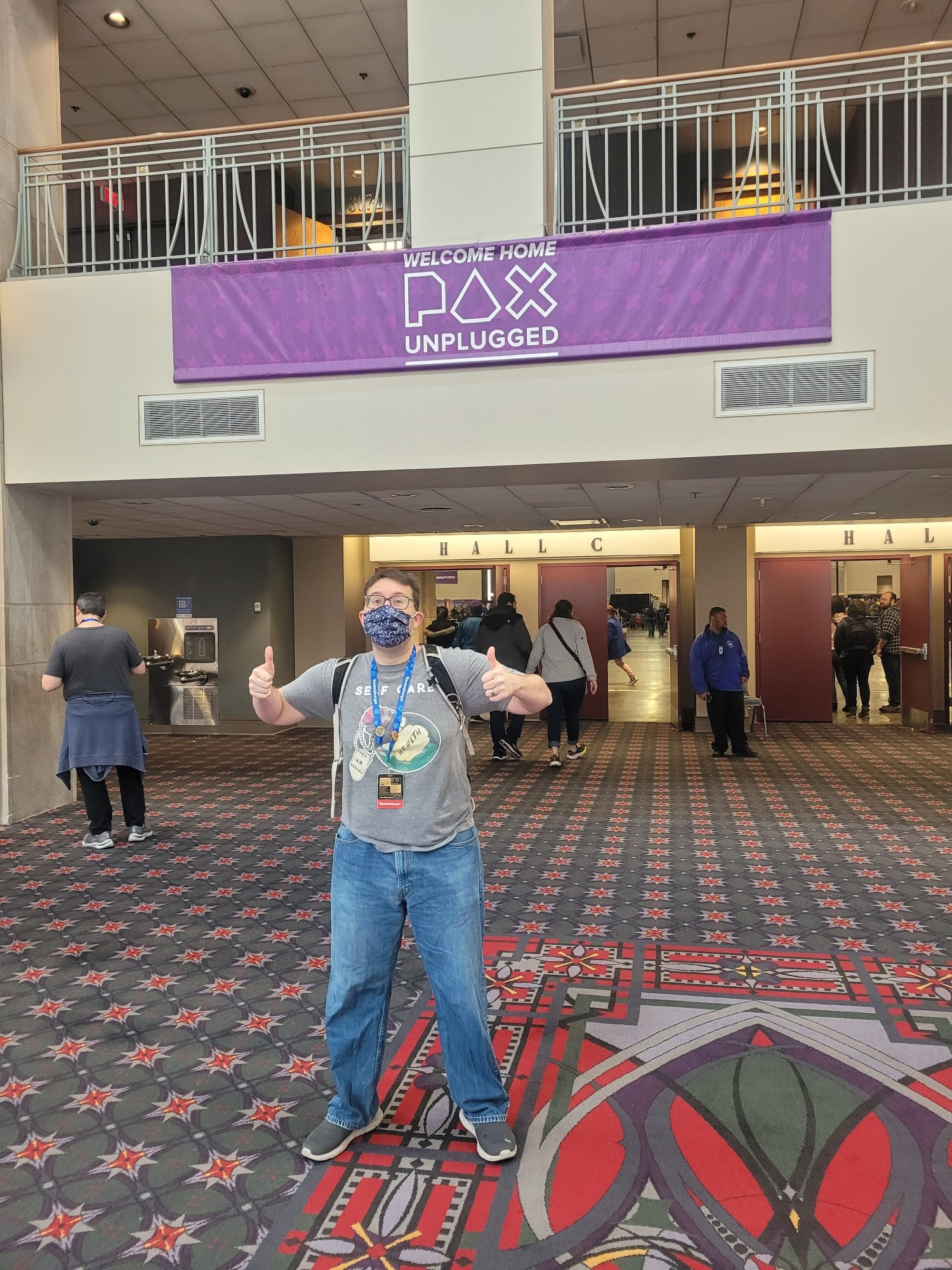 A picture of Patch standing in front of a banner that reads "Welcome Home PAX Unplugged"