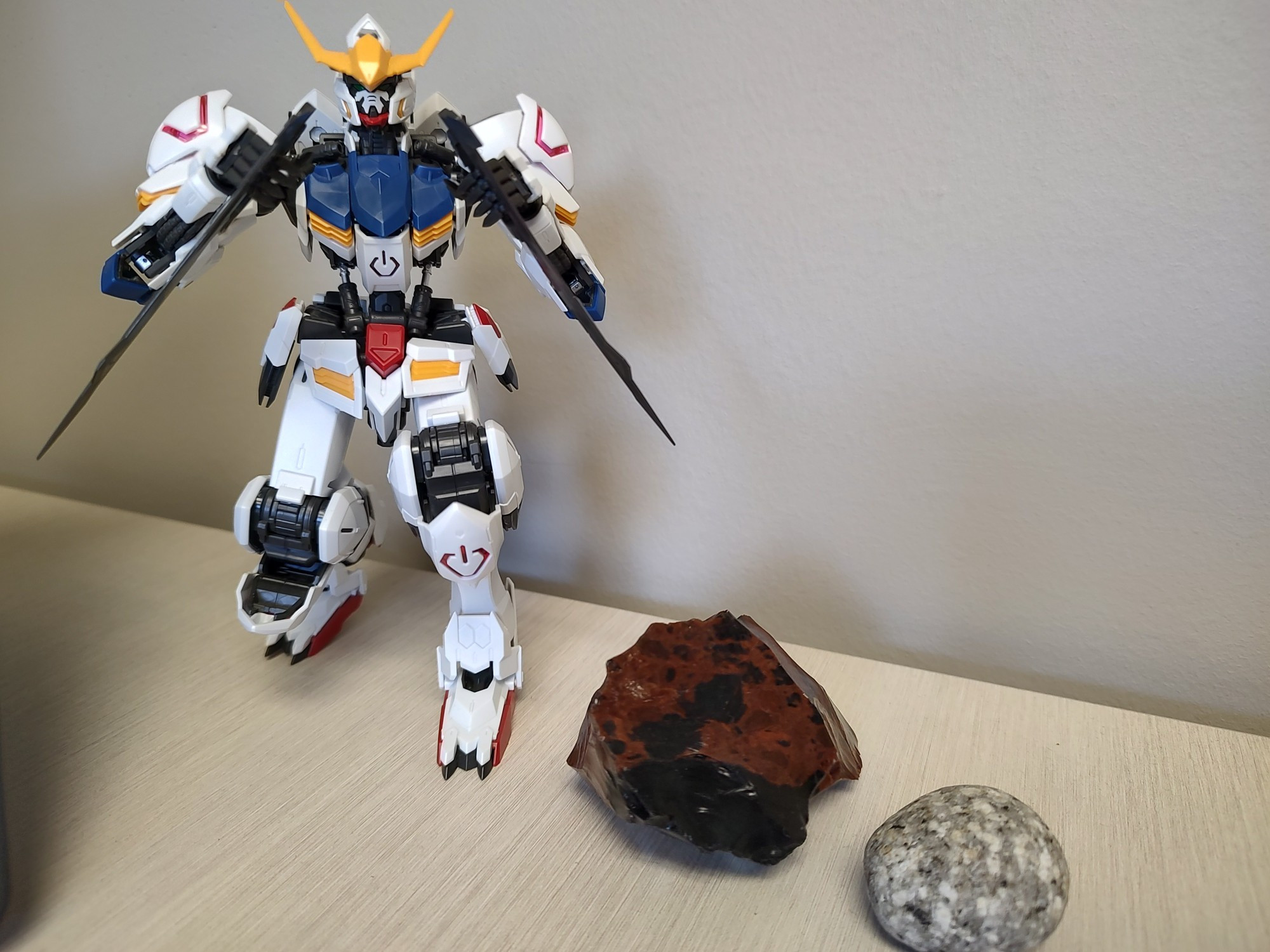 A picture of two rocks, a mahogany obsidian and a small, round piece of glaciated granite, next to the Master Grade Gundam Barbatos Gunpla kit.