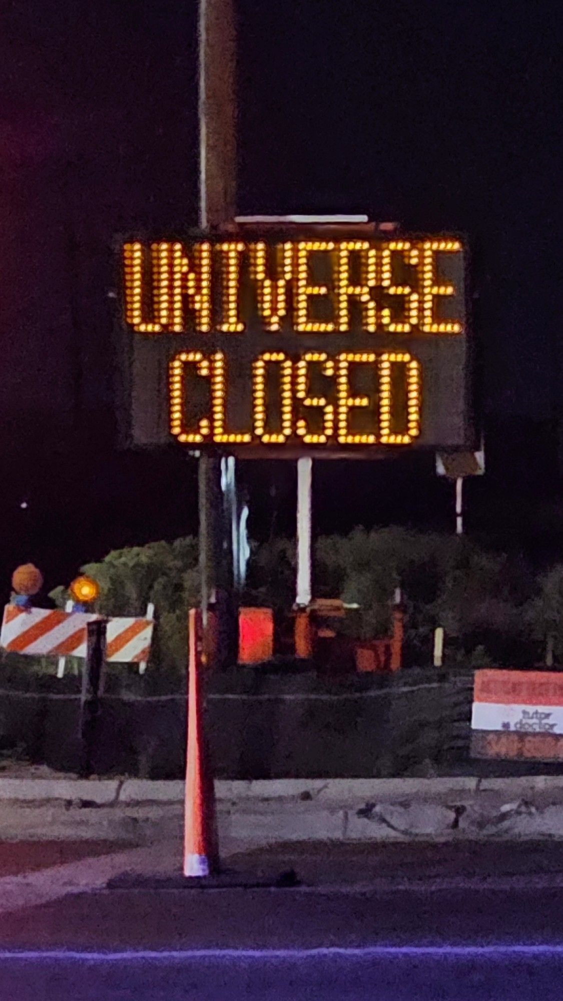 A construction zone at night, with a large LED sign that says, "UNIVERSE CLOSED."