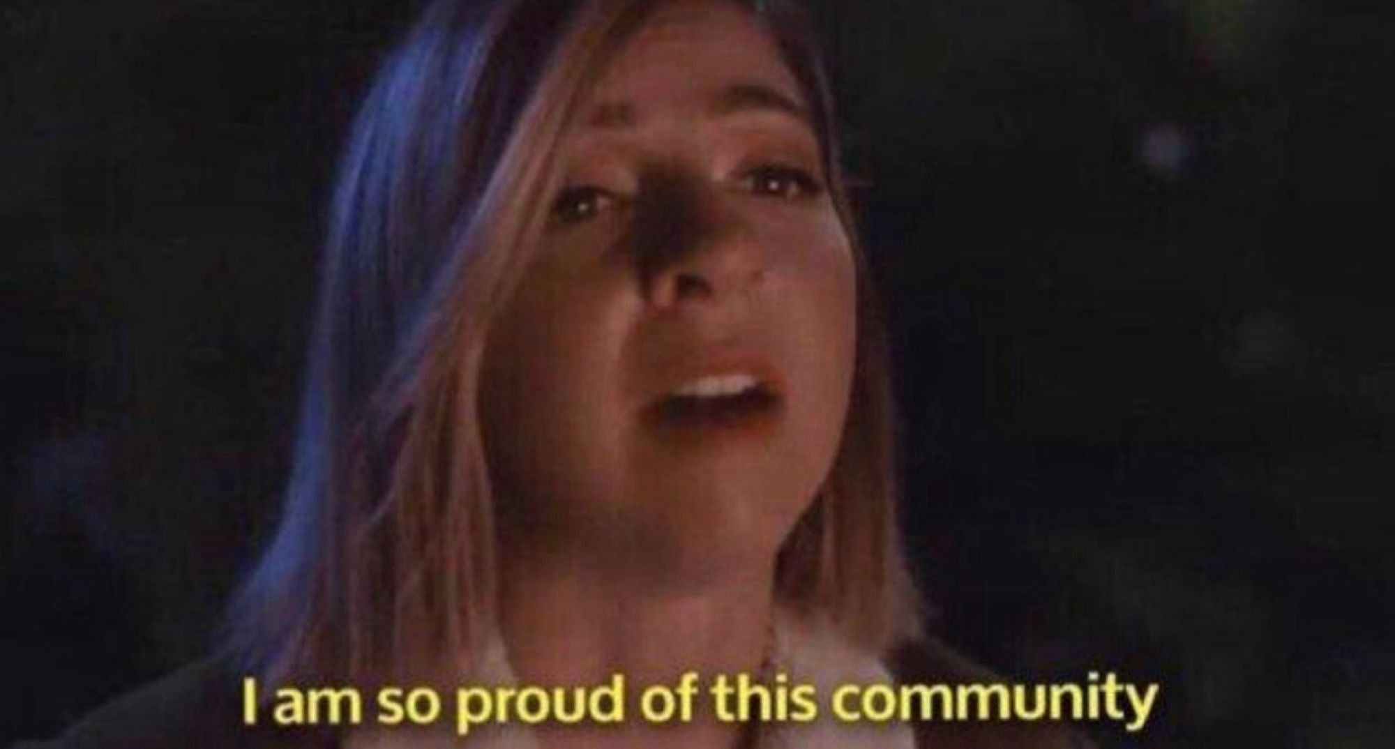 Video still of a young woman in her 20s sitting in exterior light at night with subtitles that read “I am so proud of this community”