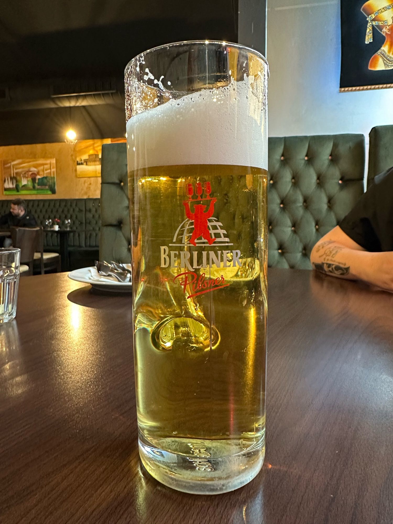 A glass of Berliner beer in a wooden table in a plush bar, a tattooed arm on the edge of the table