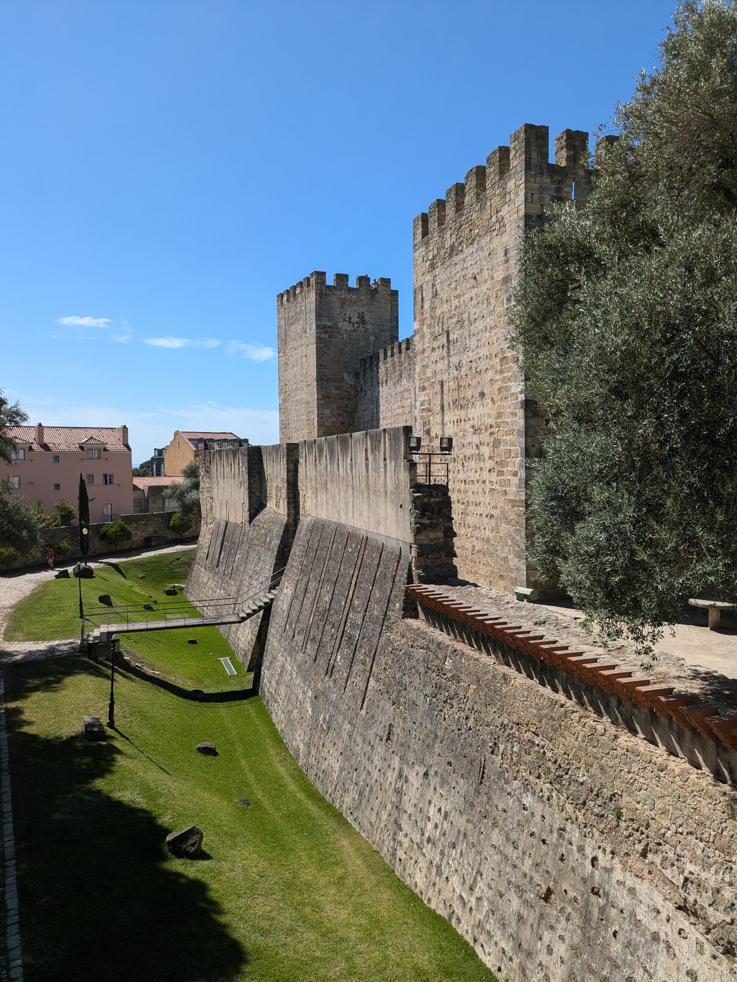 Imposing tan castle walls and towers against a bright blue sky. Lisbon, Portugal.