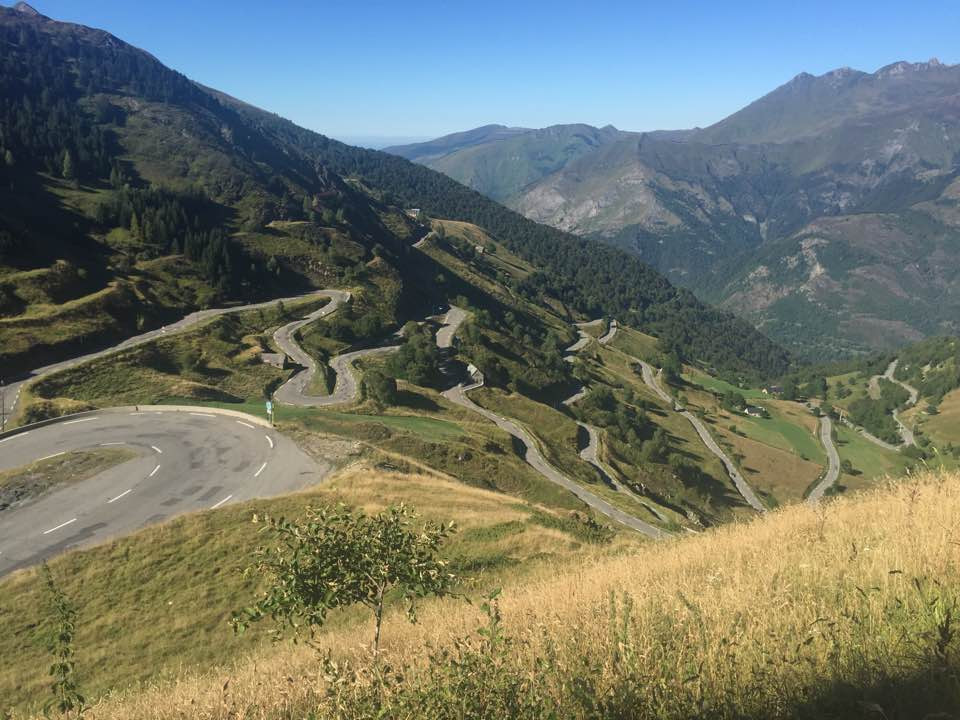 A mountain road from above, showing a lot of switchback turns, and a valley in the distance.
