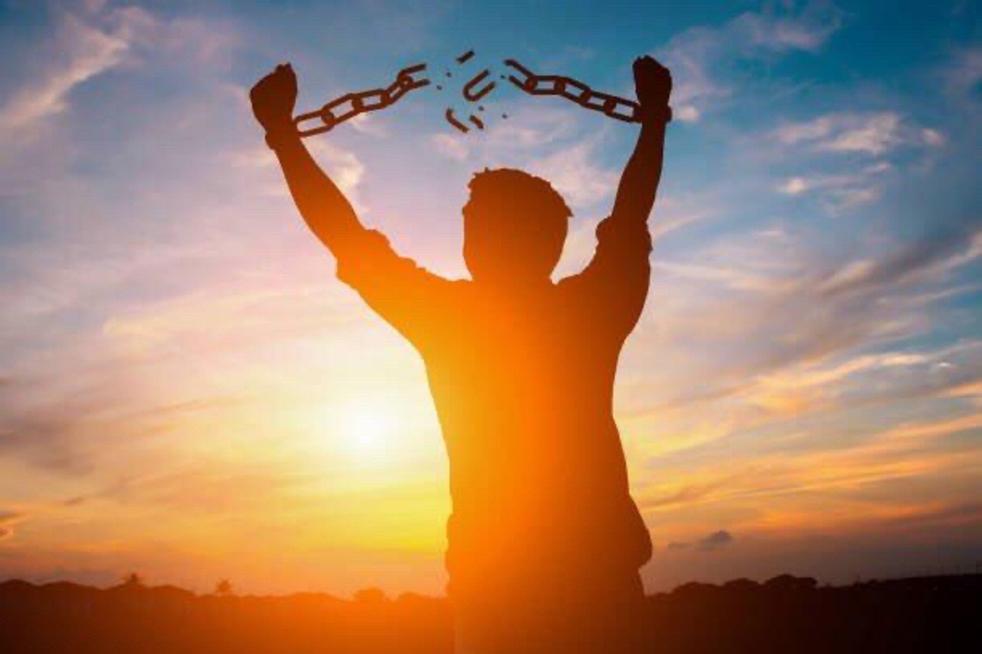 Man breaking free from his chains with a beautiful sunset